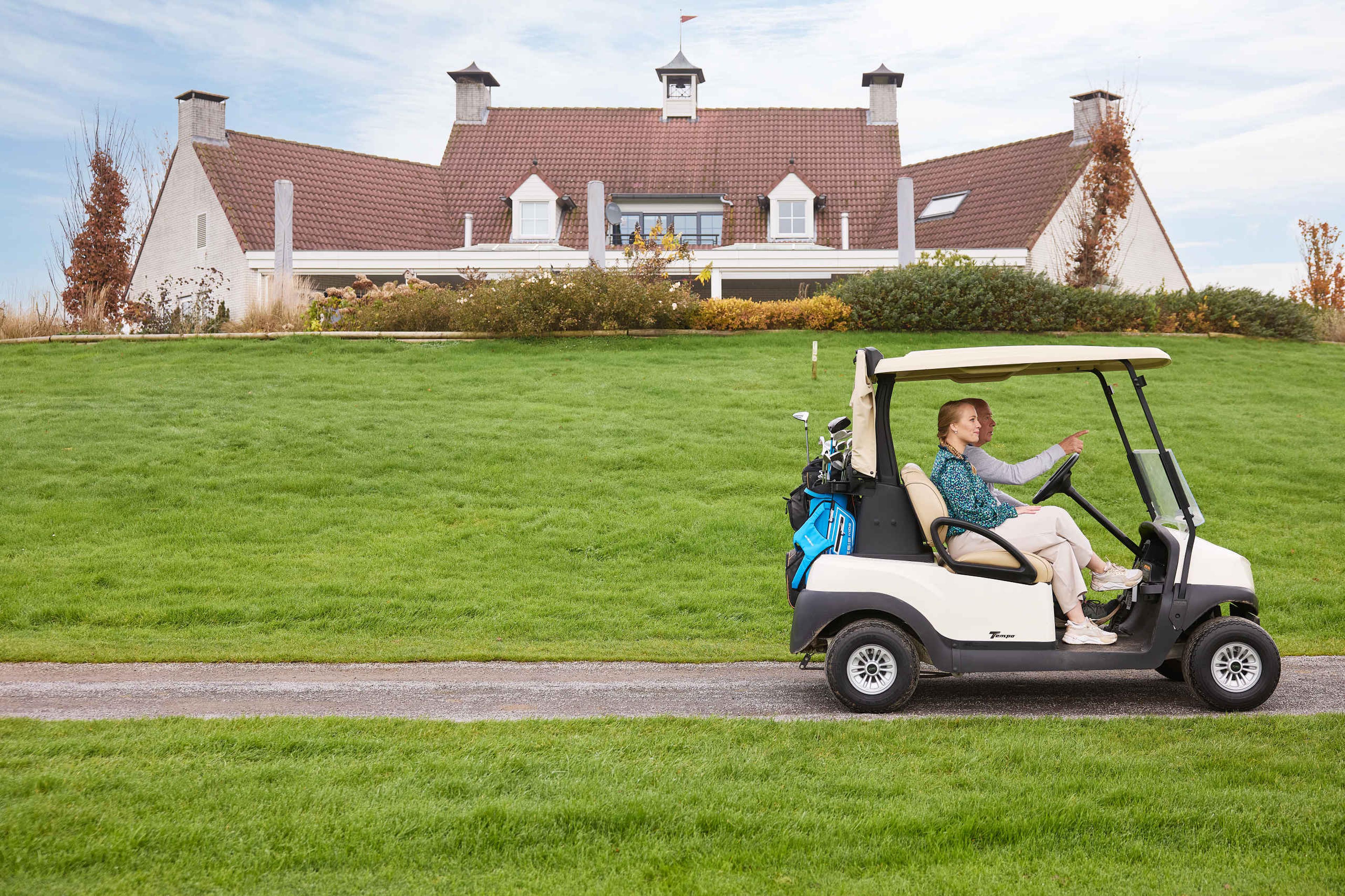 Vader en dcchter in golfkar met restaurant De Hooghe Bergh op de achtergrond bij Golf De Gulbergen