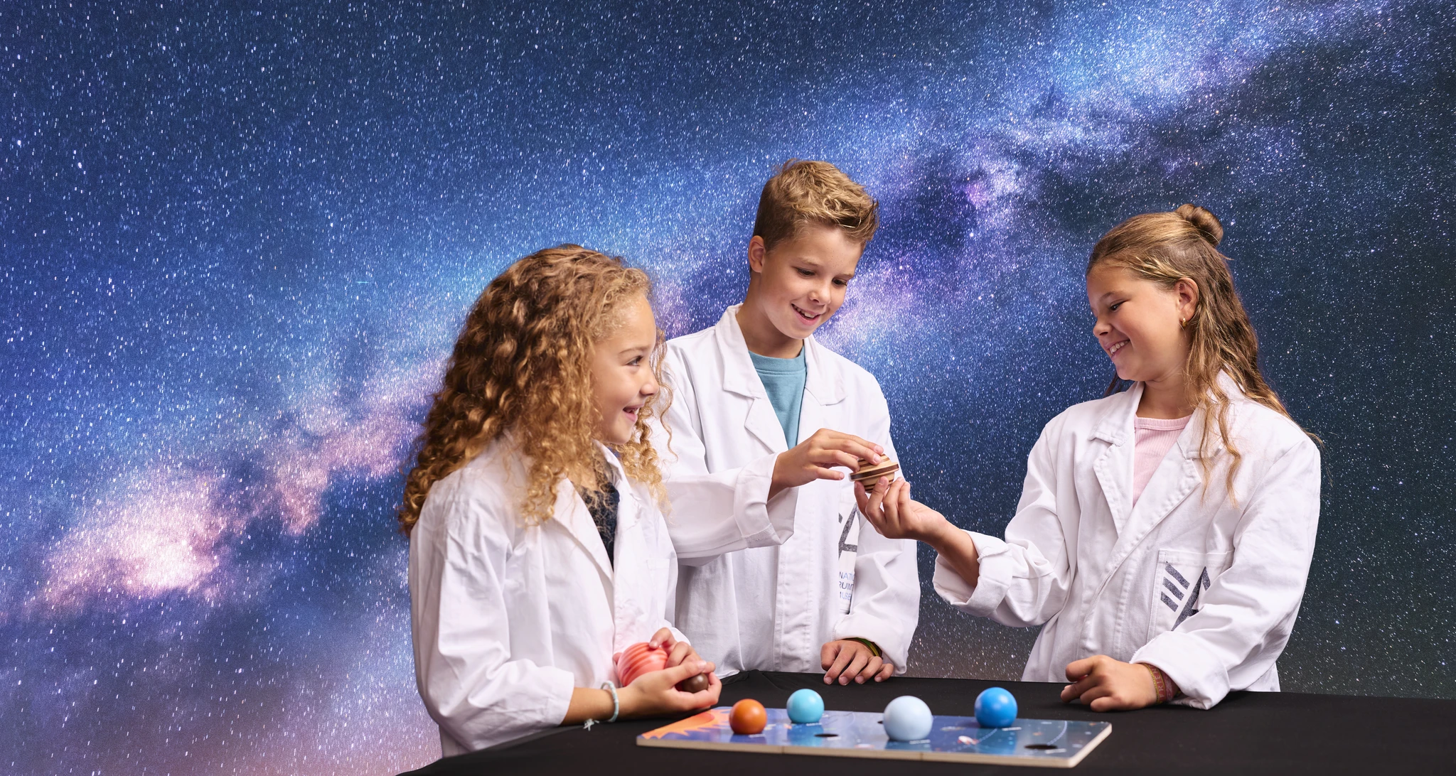 Drie kinderen kijken naar planeten tijdens Space College bij Luchtvaartmuseum Aviodrome.