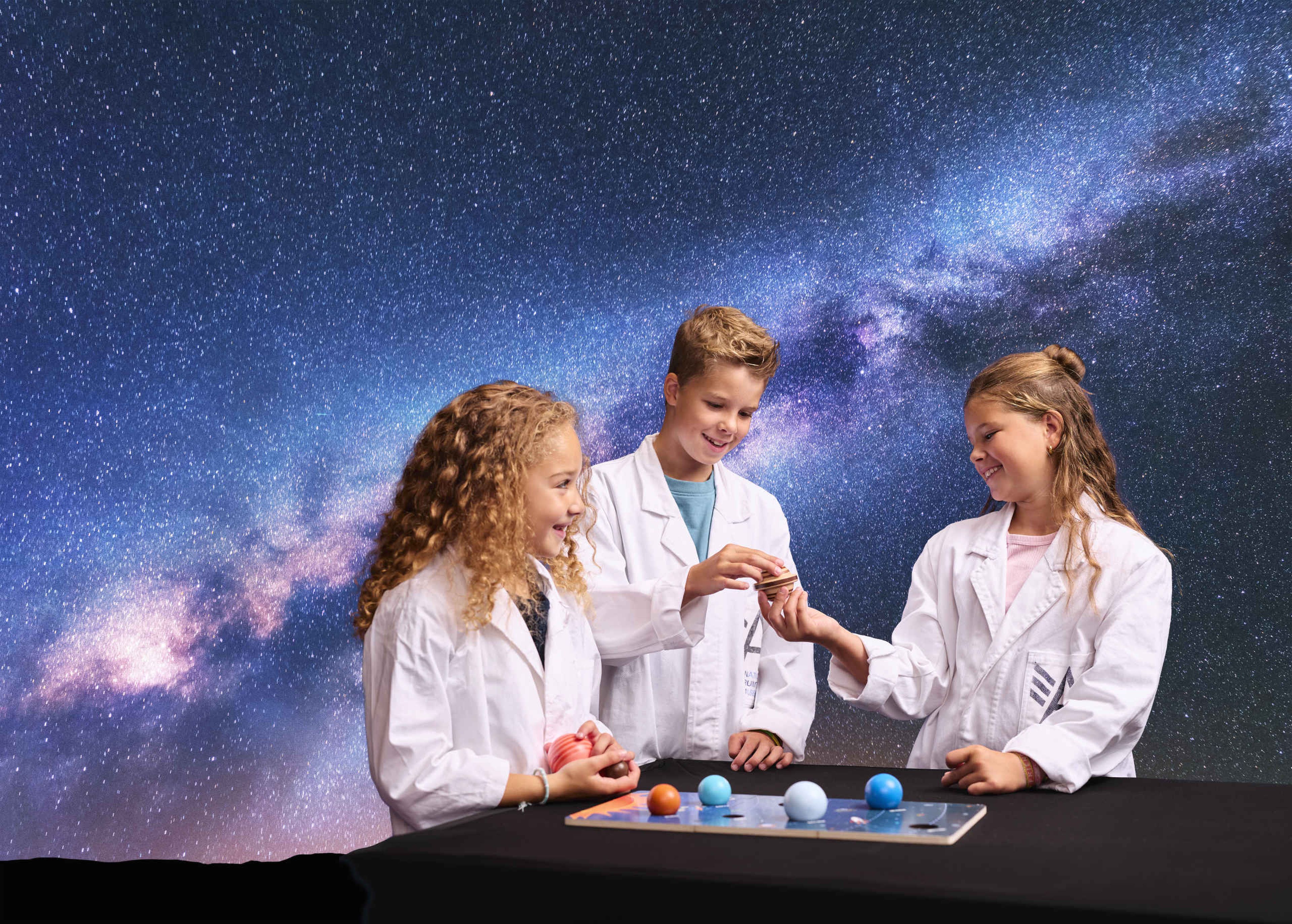 Drie kinderen kijken naar planeten tijdens Space College bij Luchtvaartmuseum Aviodrome.
