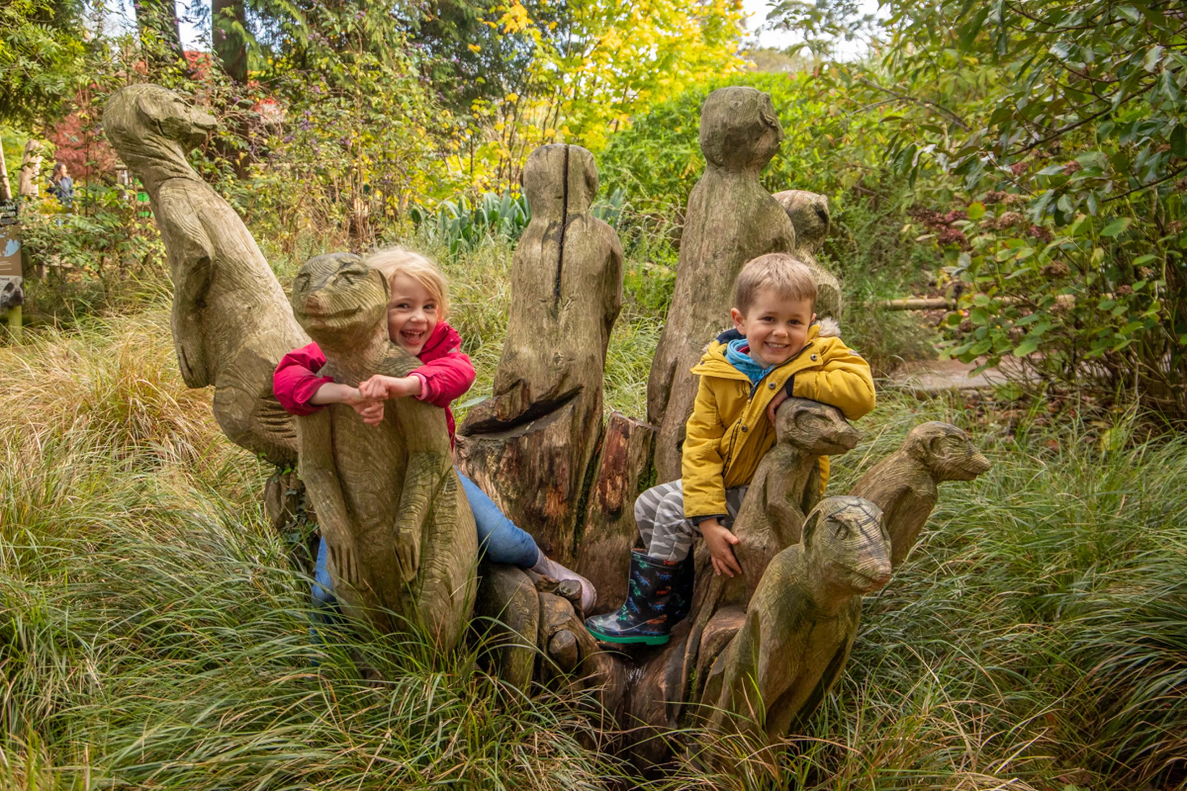 Children smiling while playing on Paignton Zoo's wooden meerkat statues