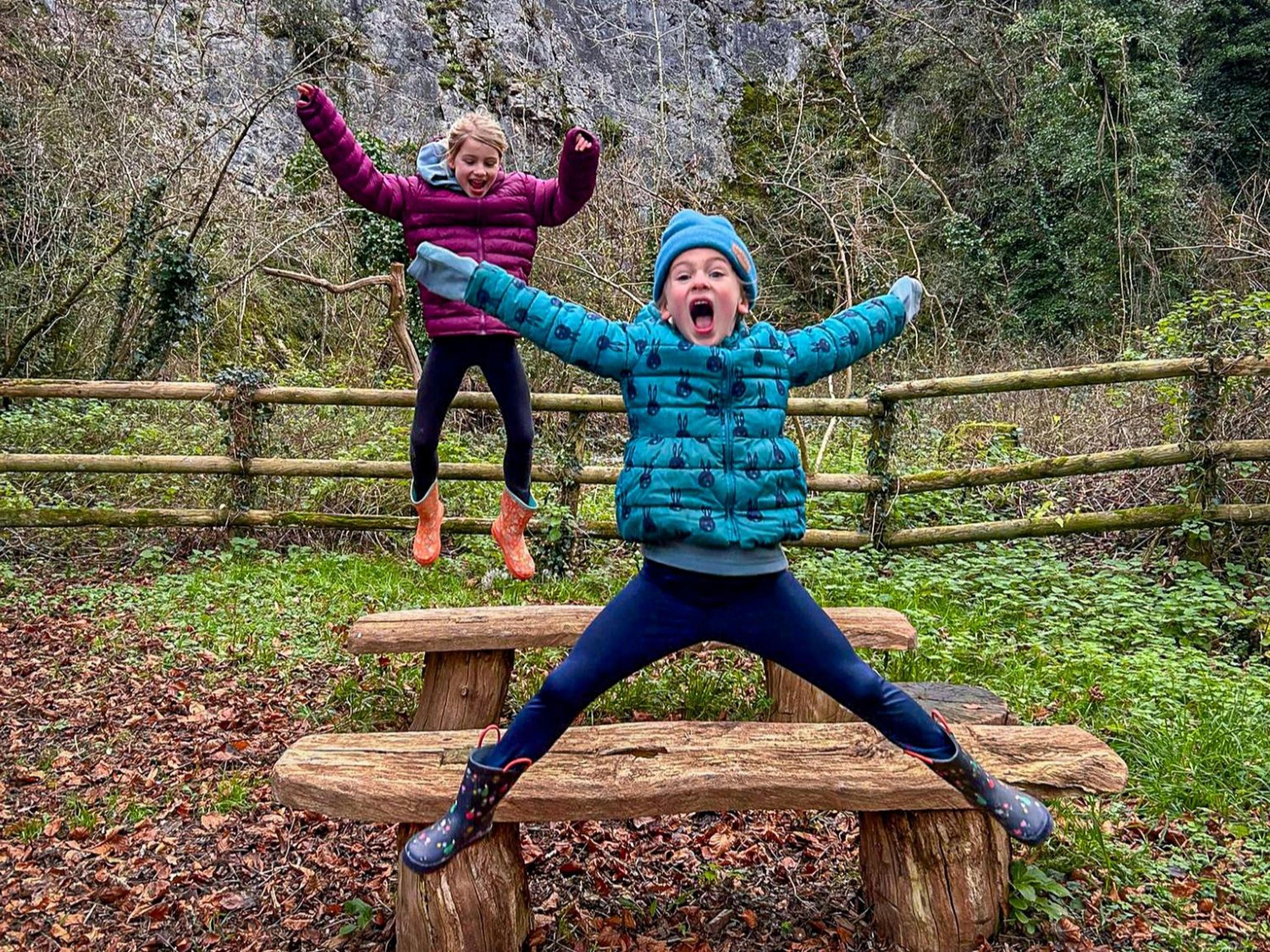 Two children jumping and smiling in front of the limestone quarryface at Paignton Zoo's Nature Trail