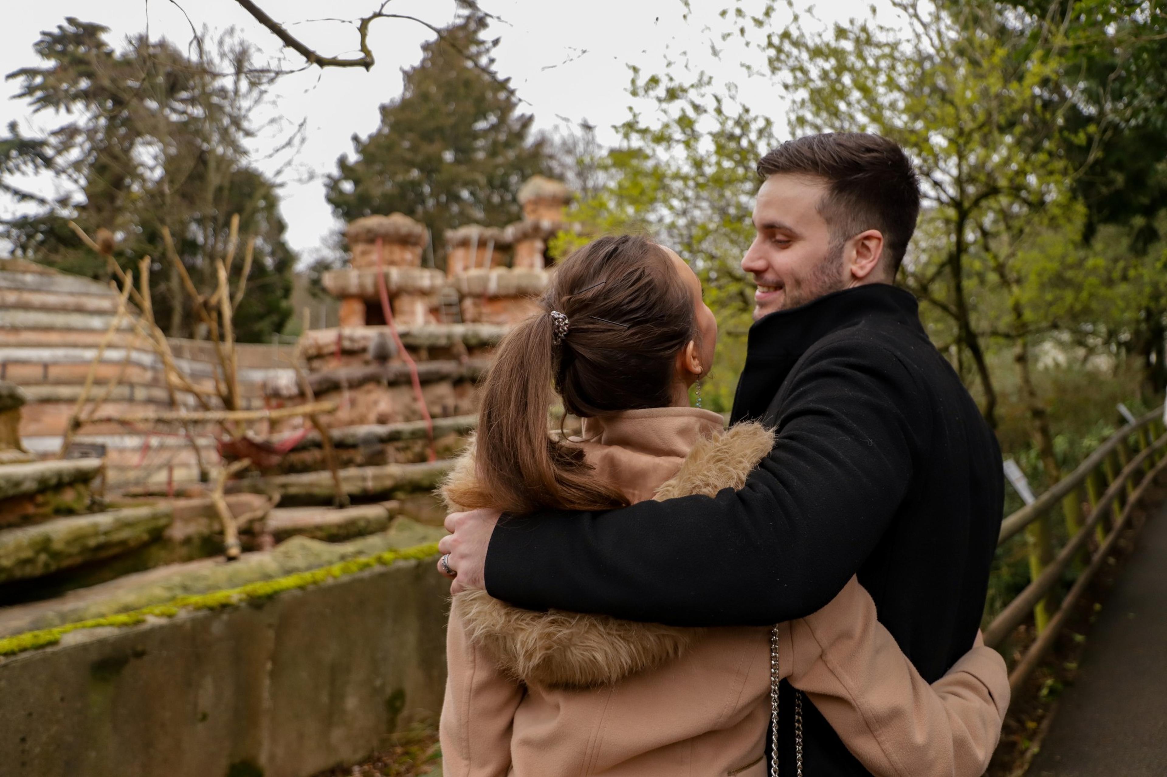 Young couple at Paignton Zoo smiling at each other while watching the Hamadryas baboons on Baboon Rock