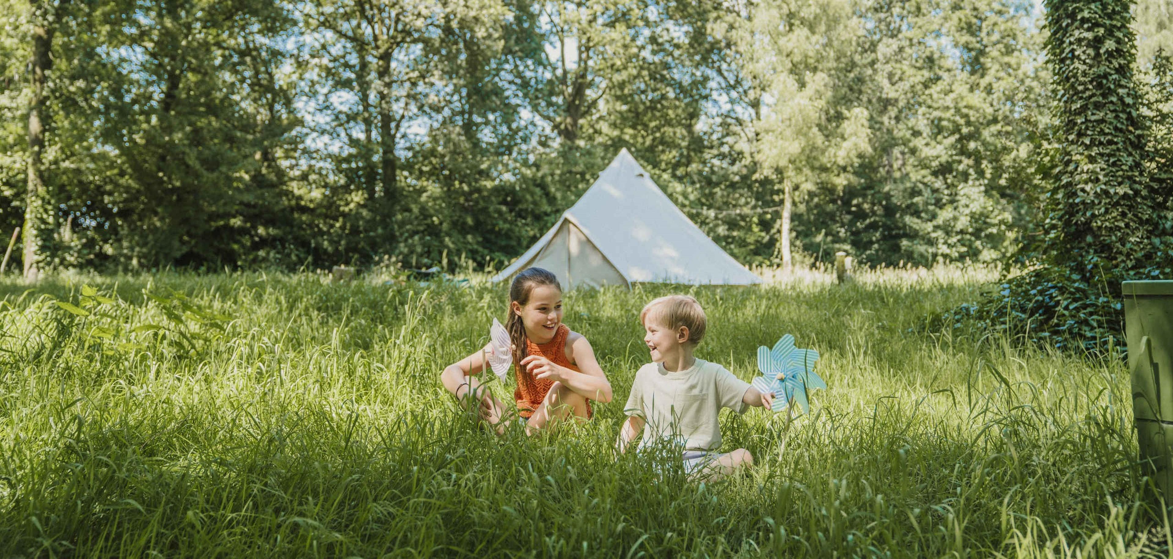 Twee kinderen spelen in het gras bij belevingscamping Vuurvlinder bij Vakantiepark Dierenbos