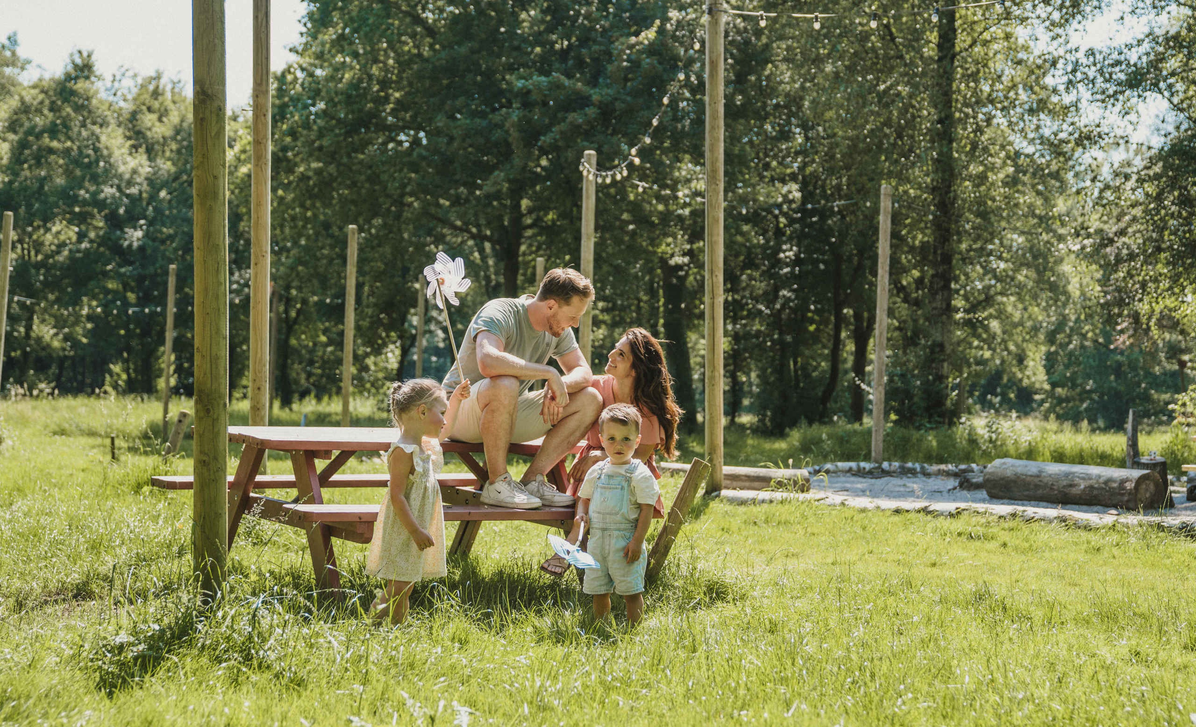 Een gezin zit aan een picknicktafel op belevingscamping vuurvlinder bij Vakantiepark Dierenbos.
