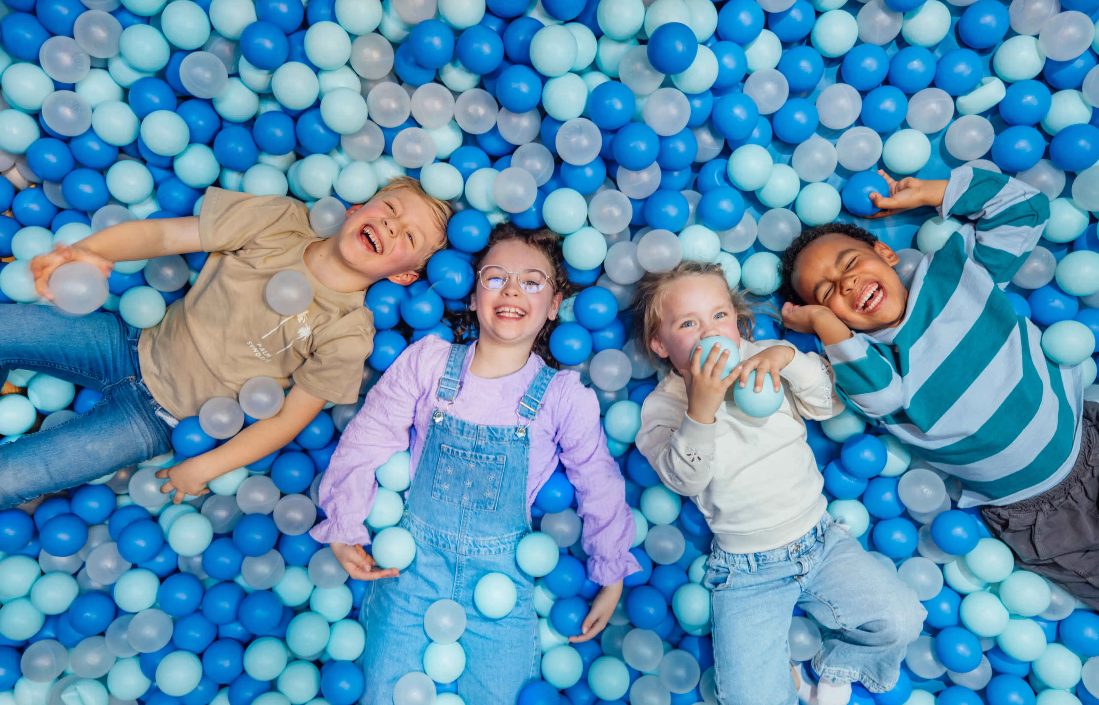 Vier kinderen liggen in de ballenbak bij Speelland Indoor