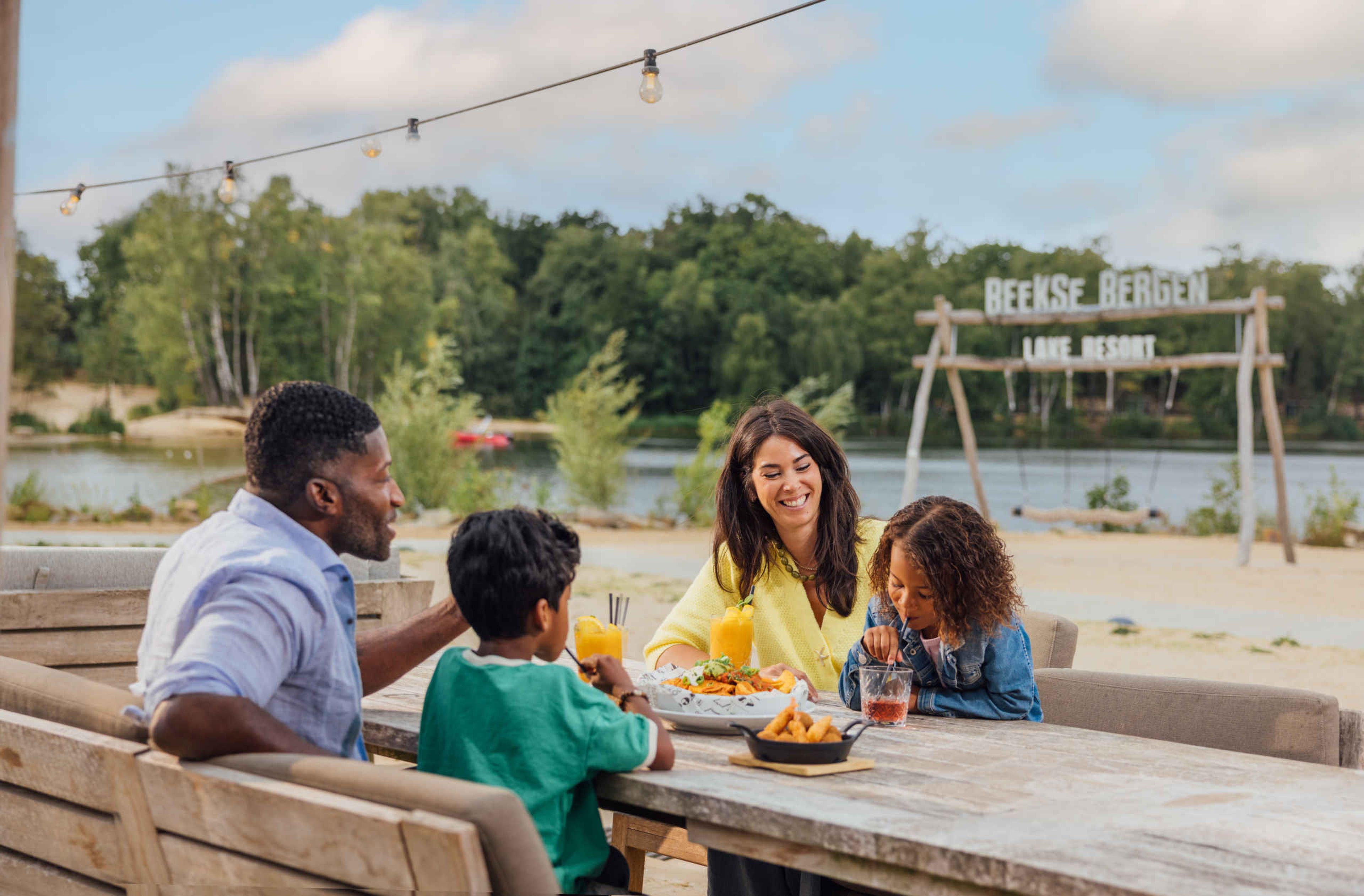 Een gezin dineert aan het strand bij Restaurant Labadi op Lake Resort Beekse Bergen.