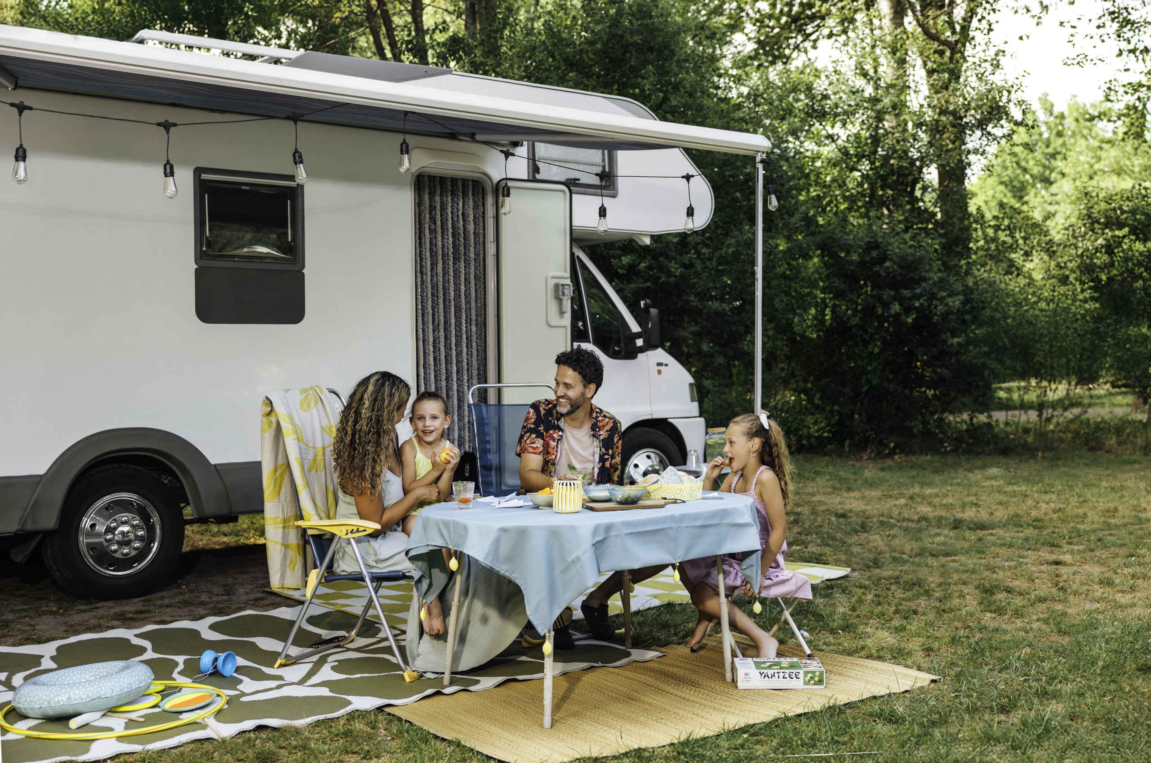 Een man en een vrouw en hun kinderen zitten bij hun camper op de camping bij Lake Resort Beekse Bergen.