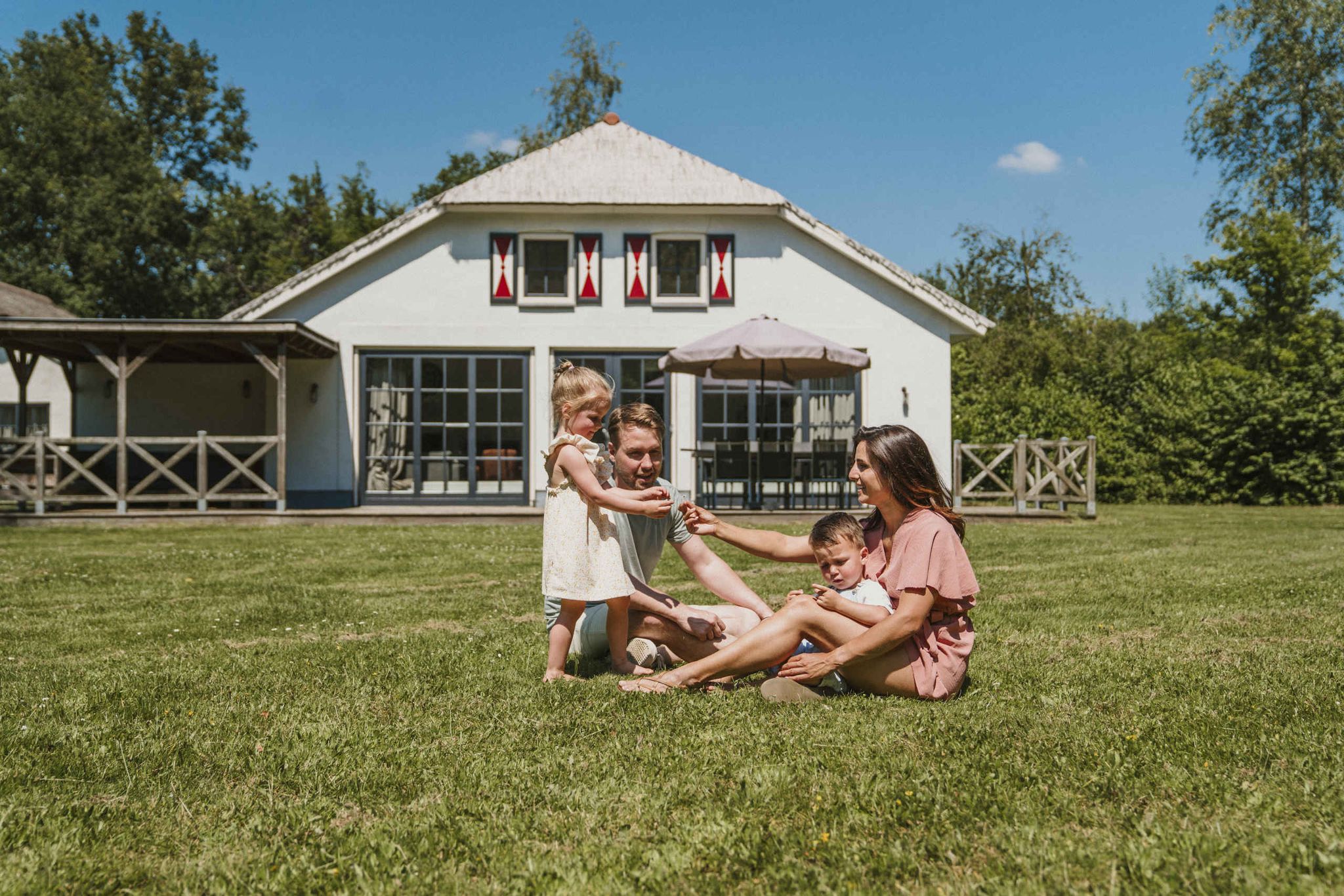 Een moeder en vader en hun kinderen spelen in het grasveld voor Villa Alpaca bij Vakantiepark Dierenbos
