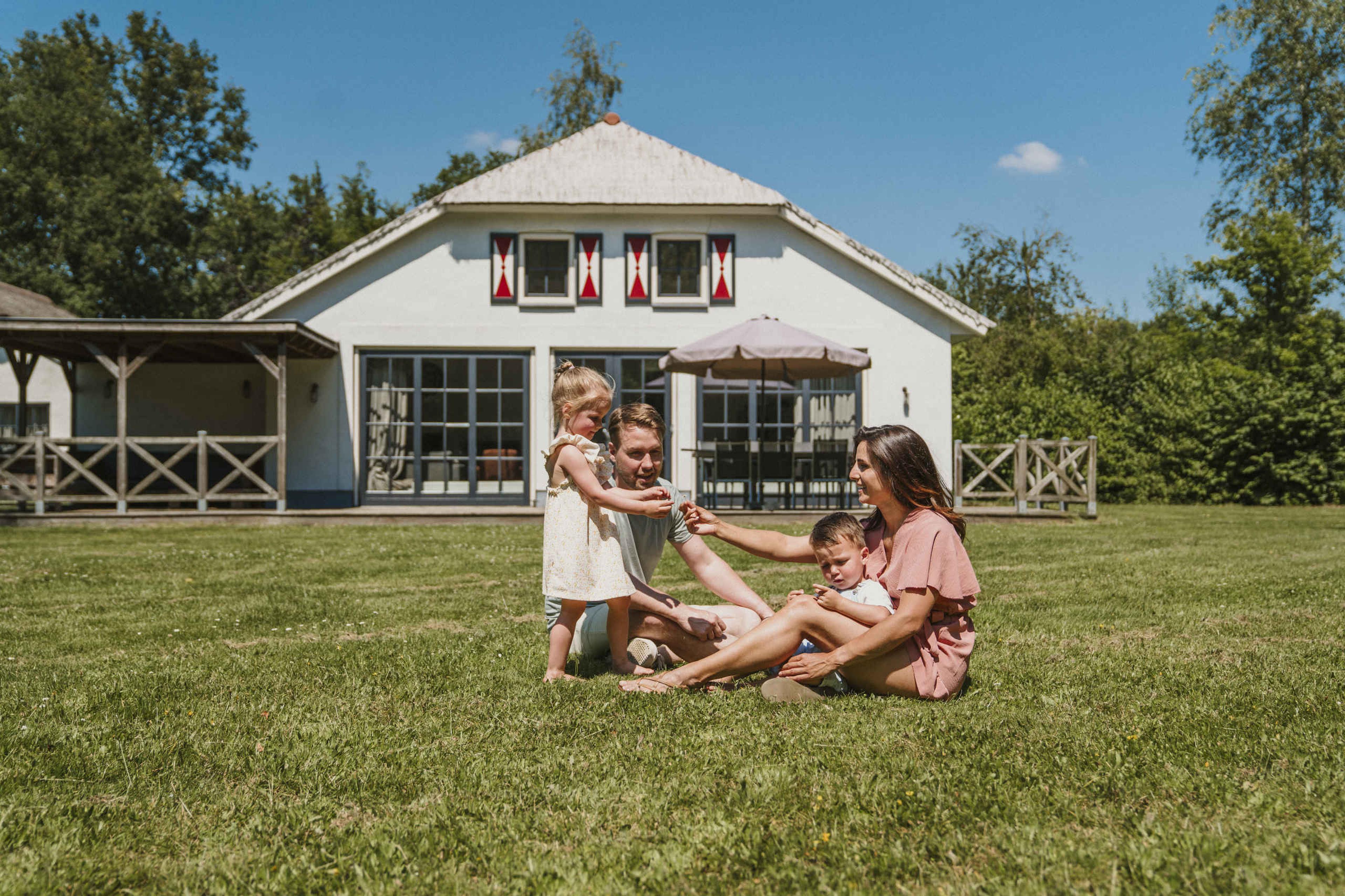 Een moeder en vader en hun kinderen spelen in het grasveld voor Villa Alpaca bij Vakantiepark Dierenbos