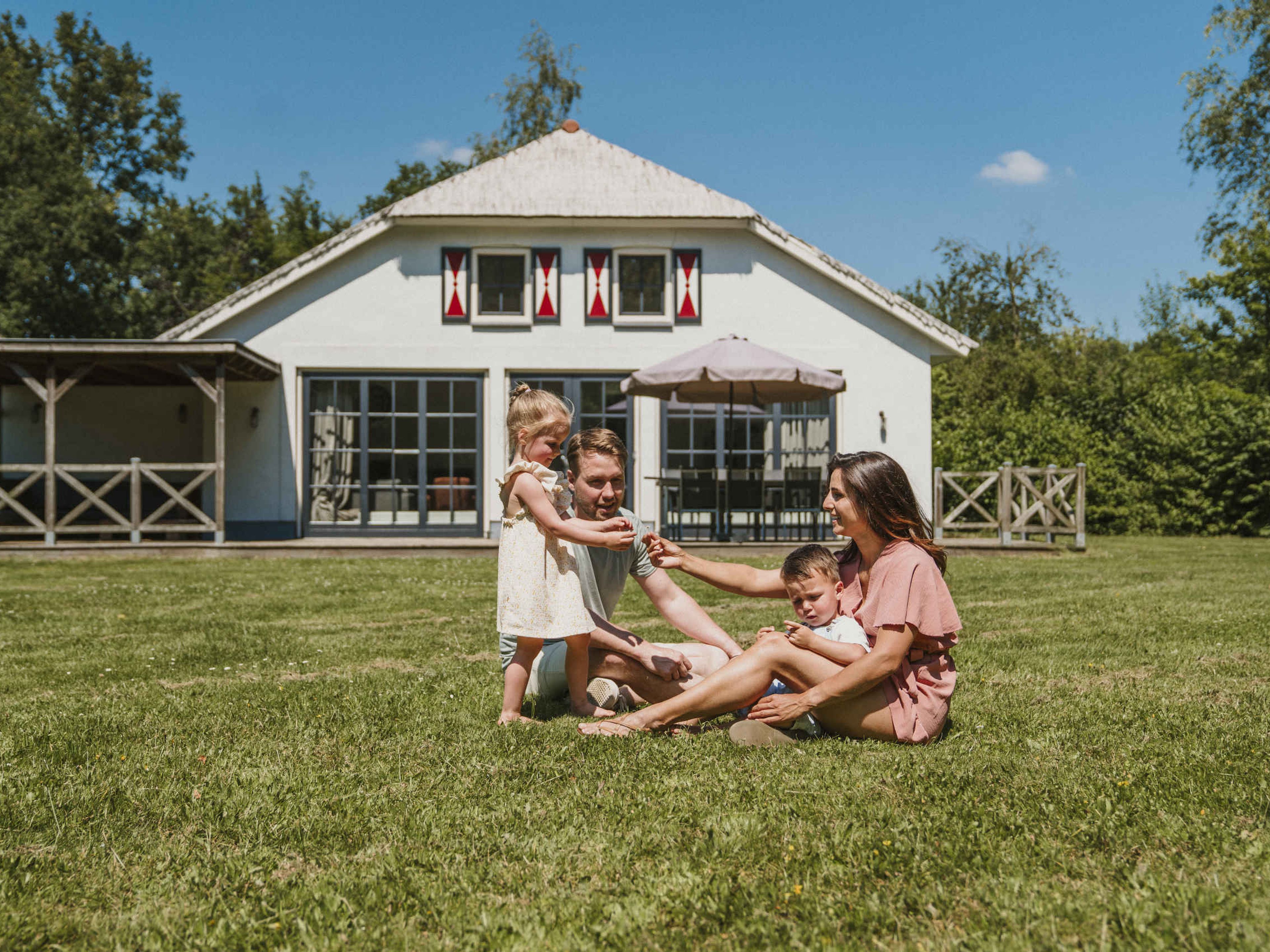 Een moeder en vader en hun kinderen spelen in het grasveld voor Villa Alpaca bij Vakantiepark Dierenbos