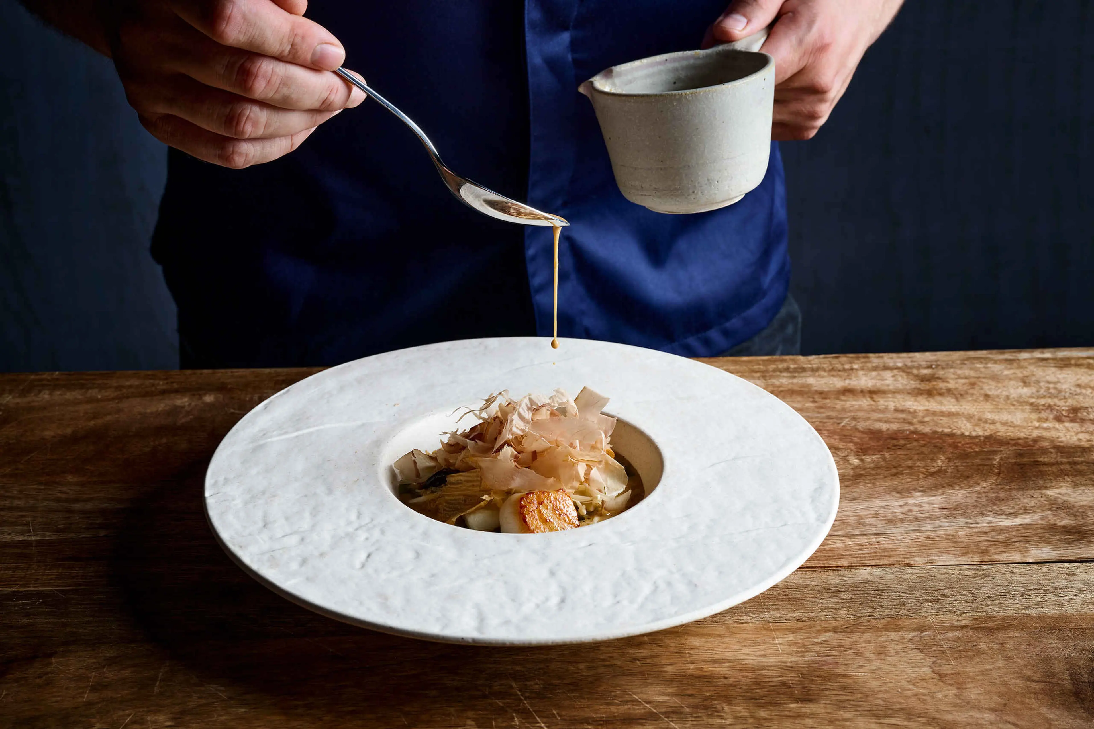 De chefkok giet de saus voorzichtig over een gerecht bij restaurant Nommos.