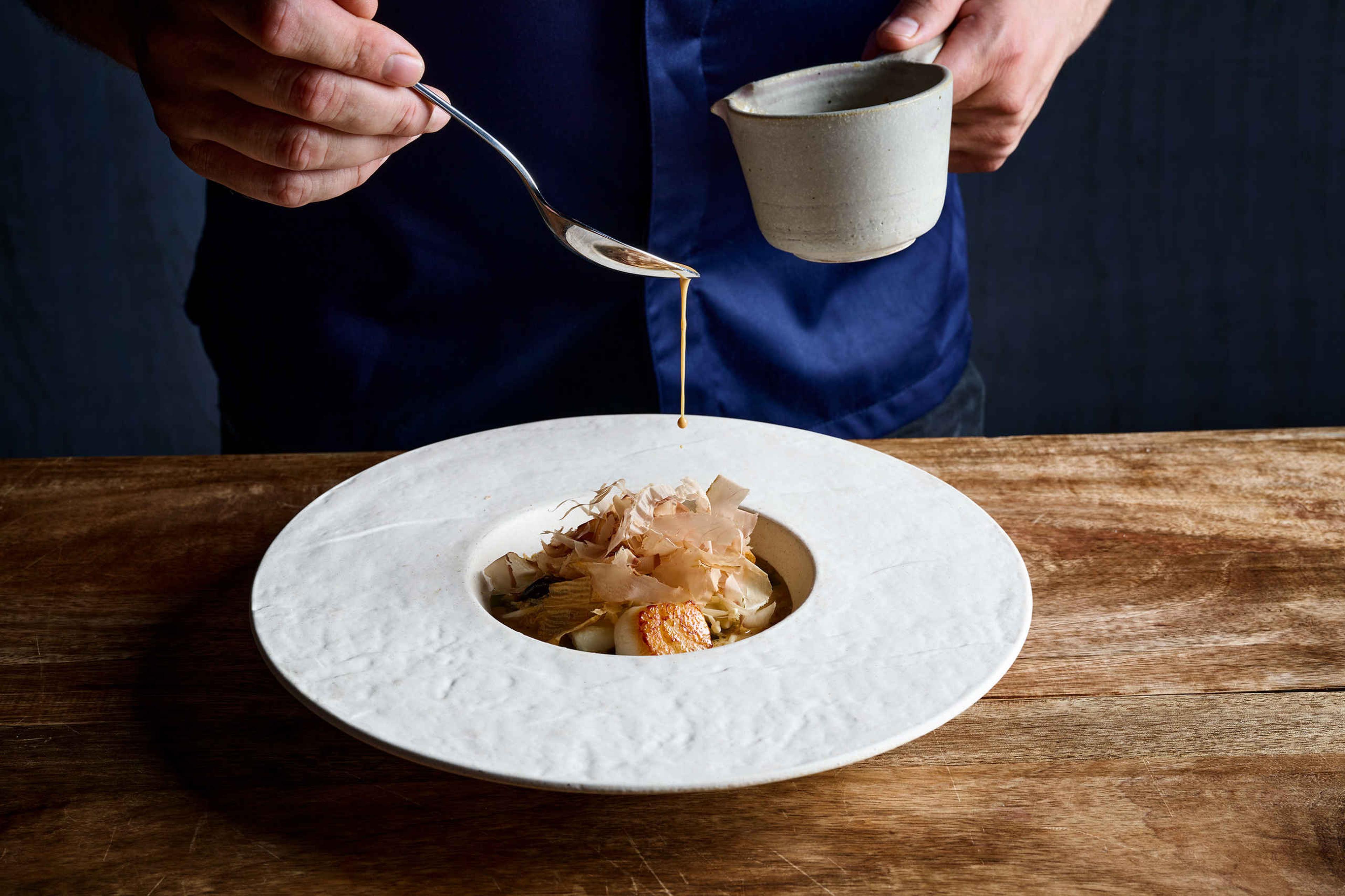 De chefkok giet de saus voorzichtig over een gerecht bij restaurant Nommos.