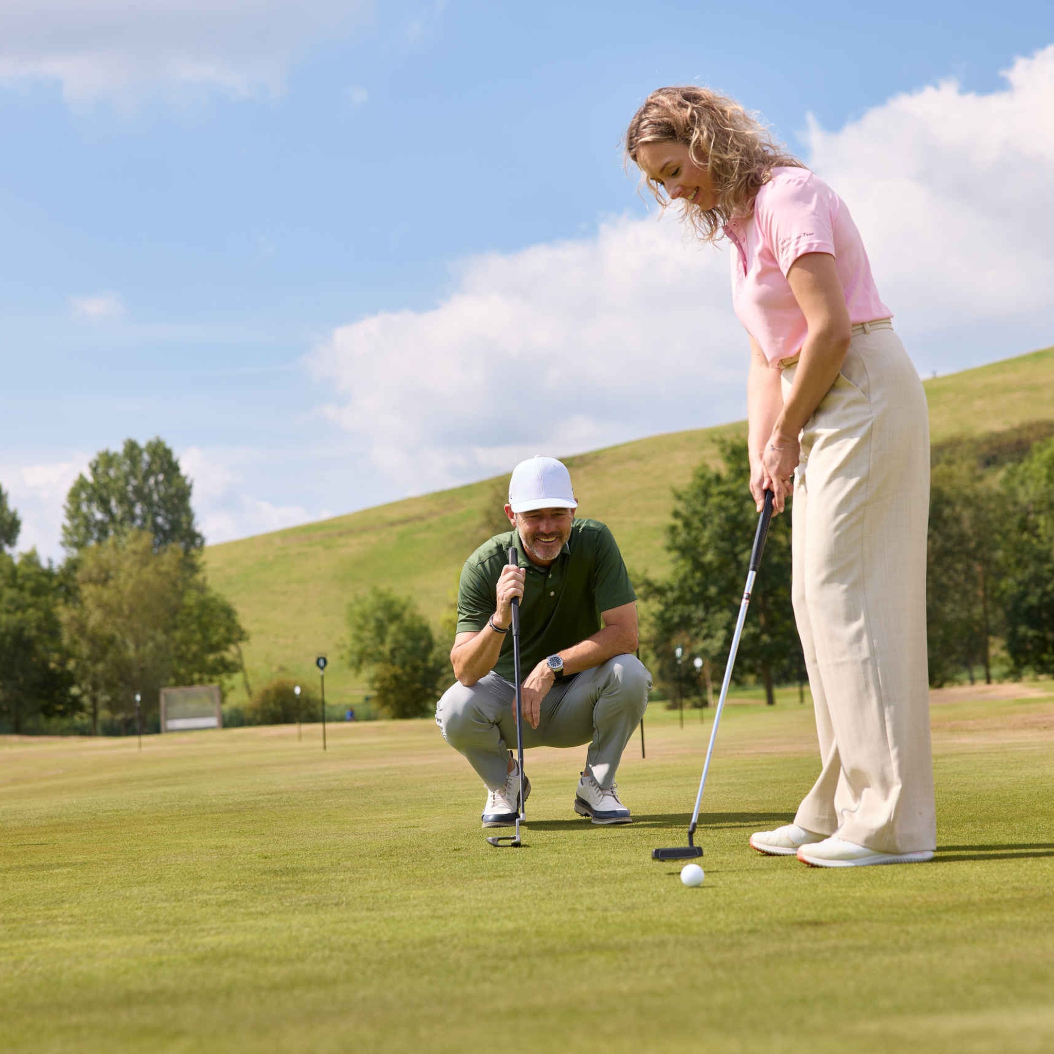 Een vrouw putt een golfbal op de puttinggreen terwijl de golfpro van Golfacademy De Gulbergen toekijkt