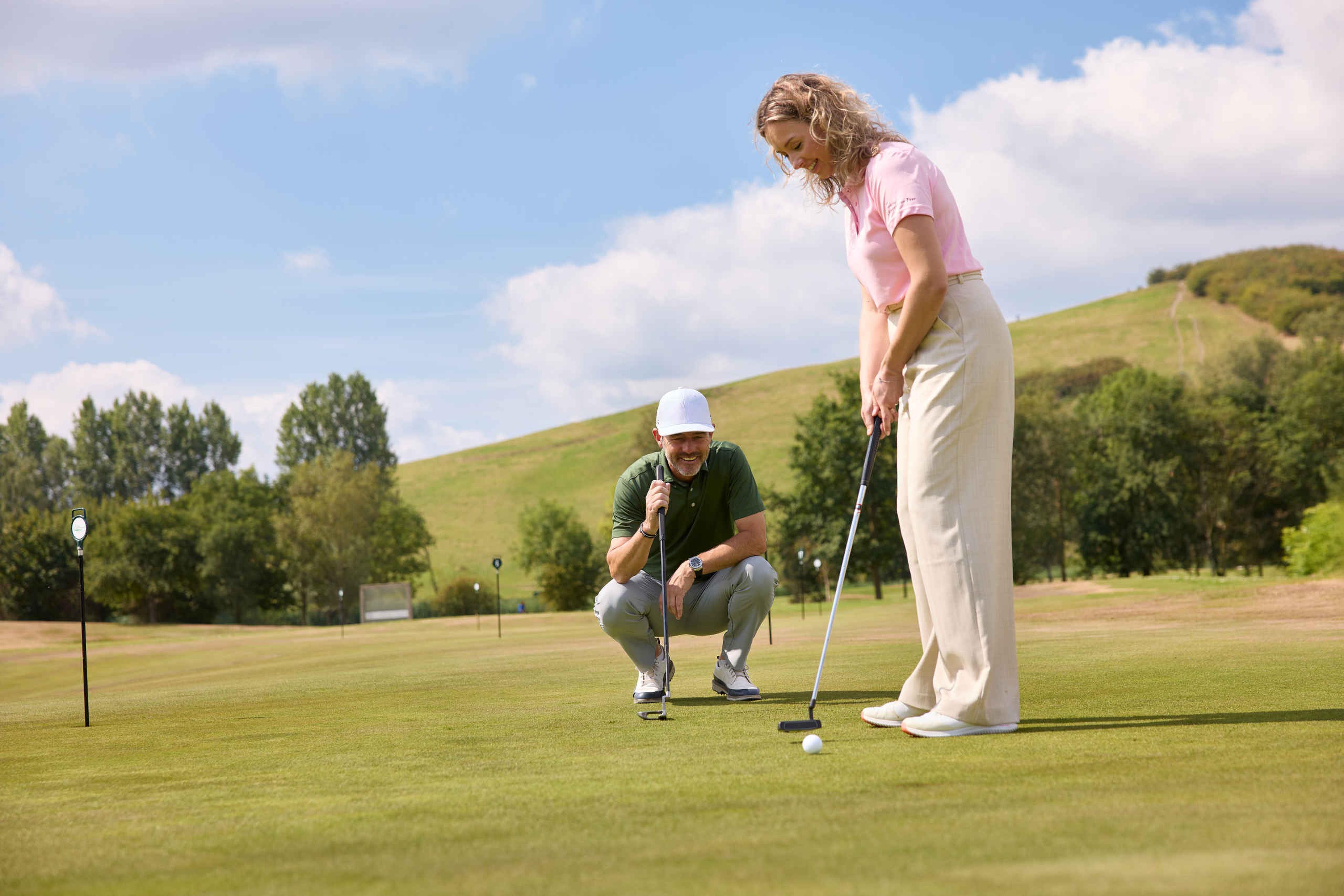 Een vrouw putt een golfbal op de puttinggreen terwijl de golfpro van Golfacademy De Gulbergen toekijkt