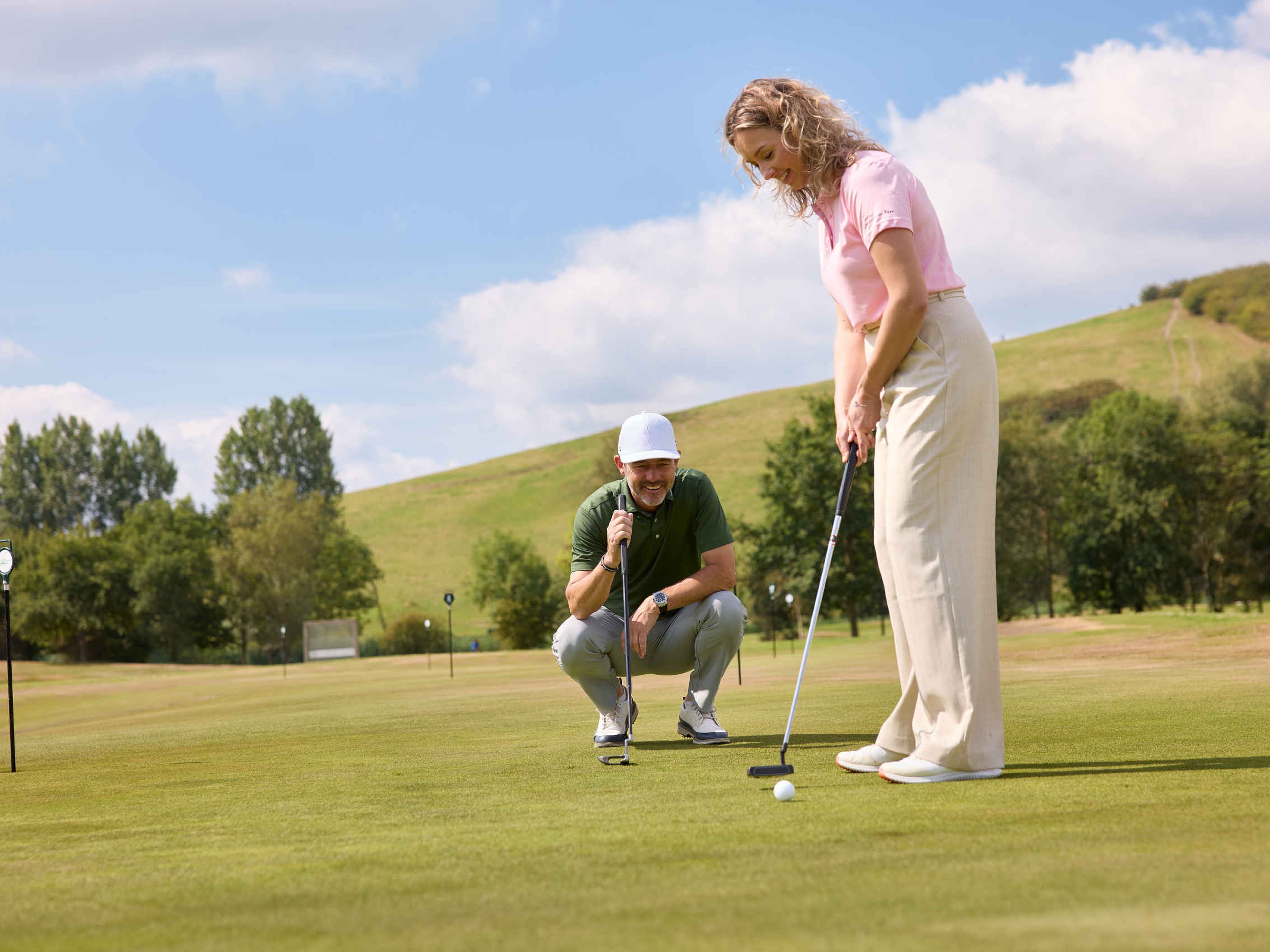 Een vrouw putt een golfbal op de puttinggreen terwijl de golfpro van Golfacademy De Gulbergen toekijkt