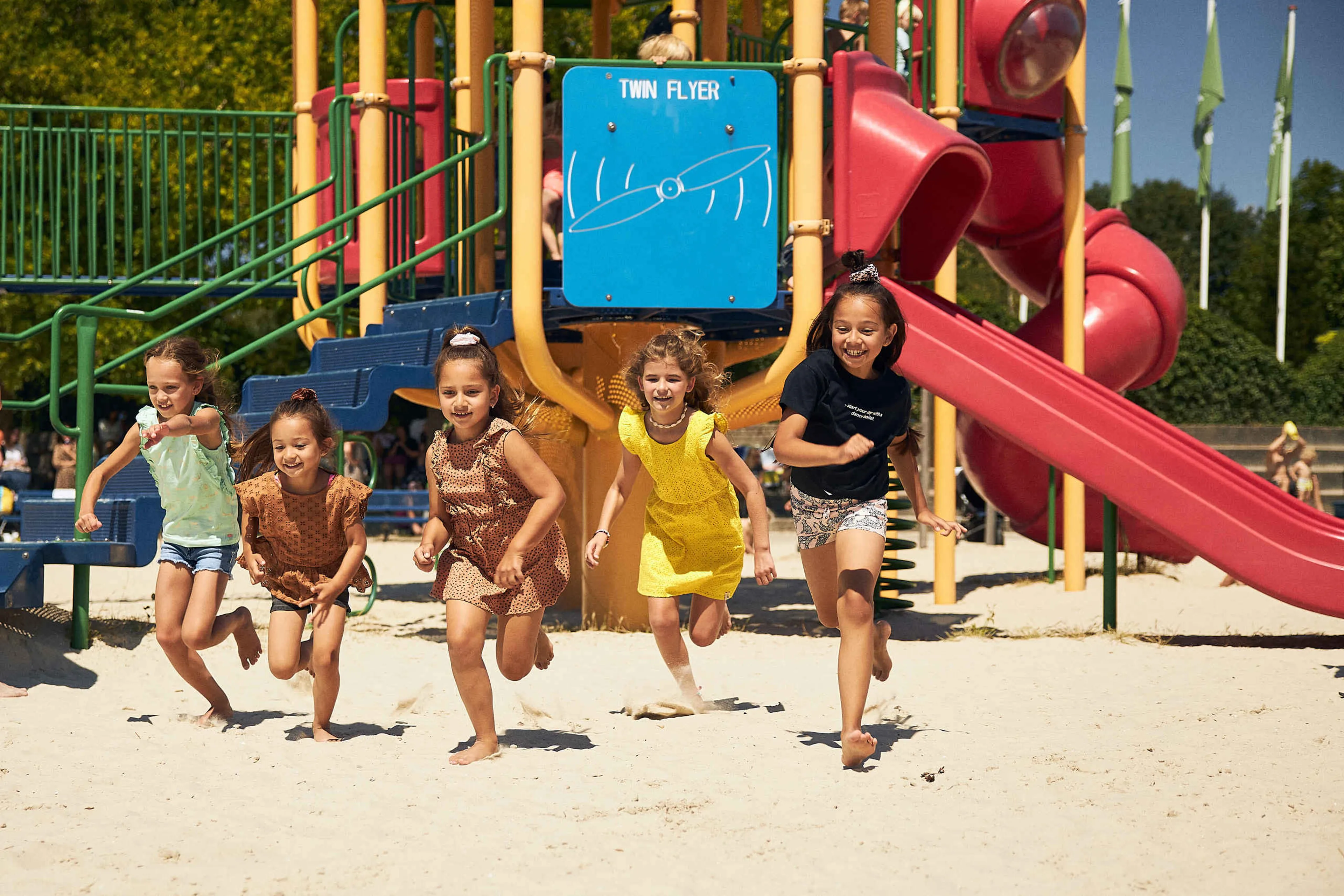 Vijf meisjes rennen over het strand langs een speeltuin bij Speelland Beekse Bergen
