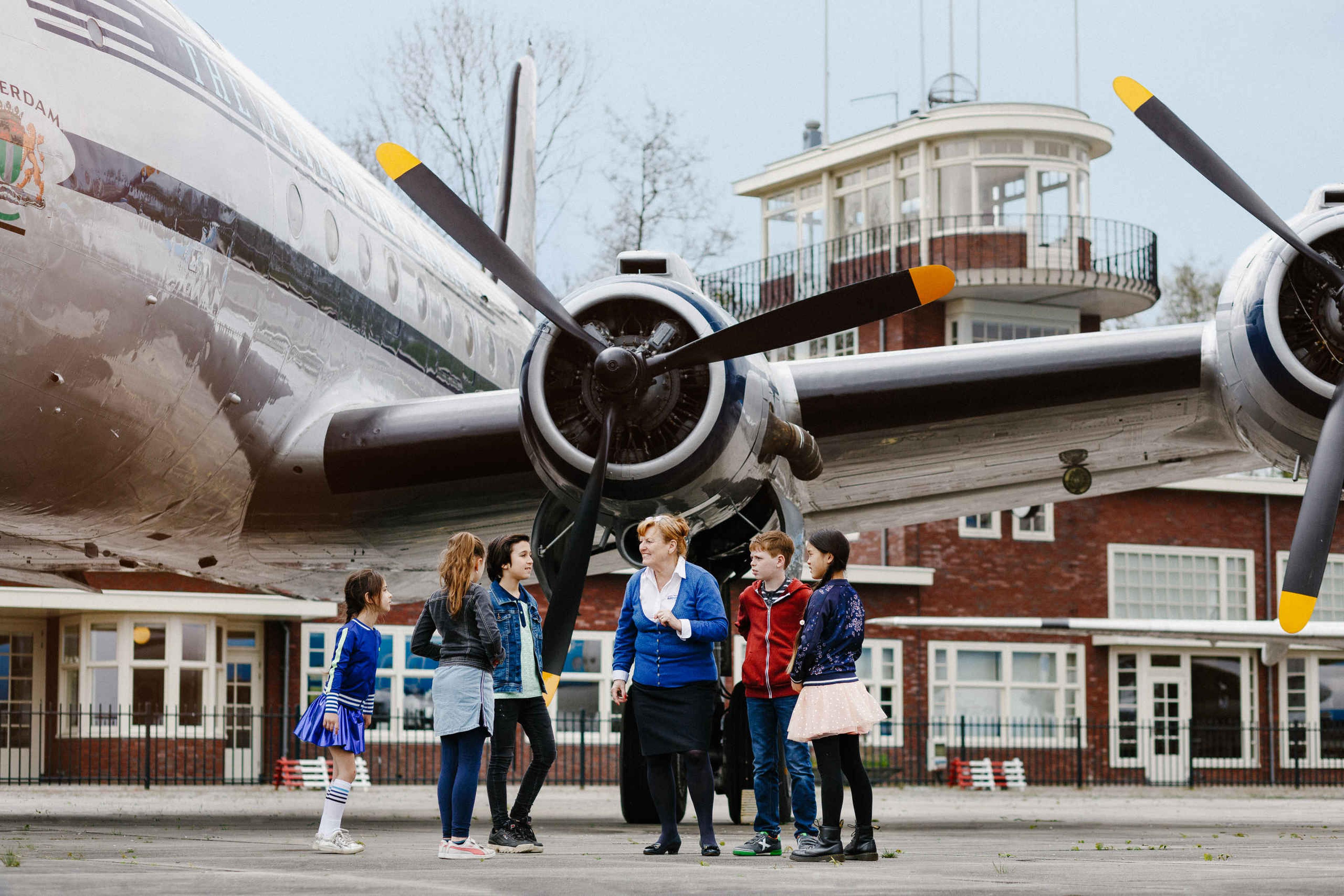 Vrijwilliger en kinderen tijdens een schoolreisje in Luchtvaartmuseum Aviodrome