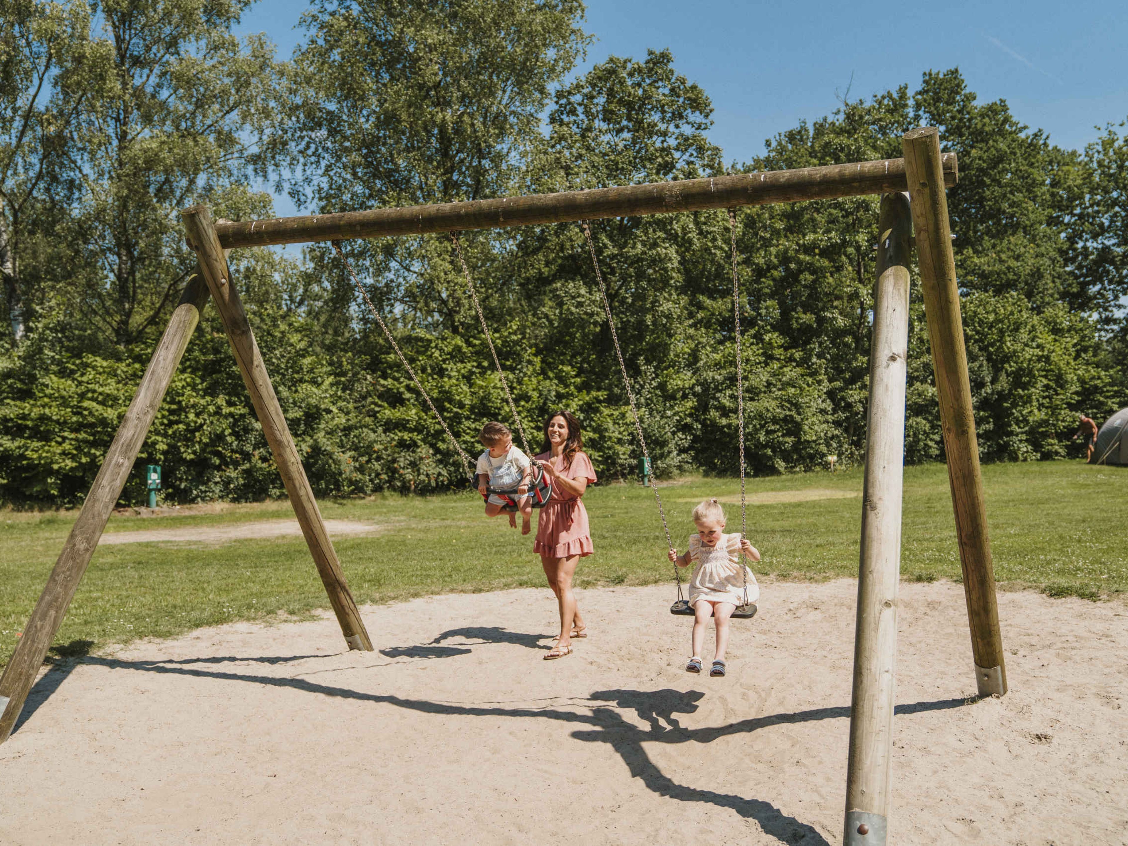Een moeder speelt met haar kinderen bij de schommels bij Vakantiepark Dierenbos.