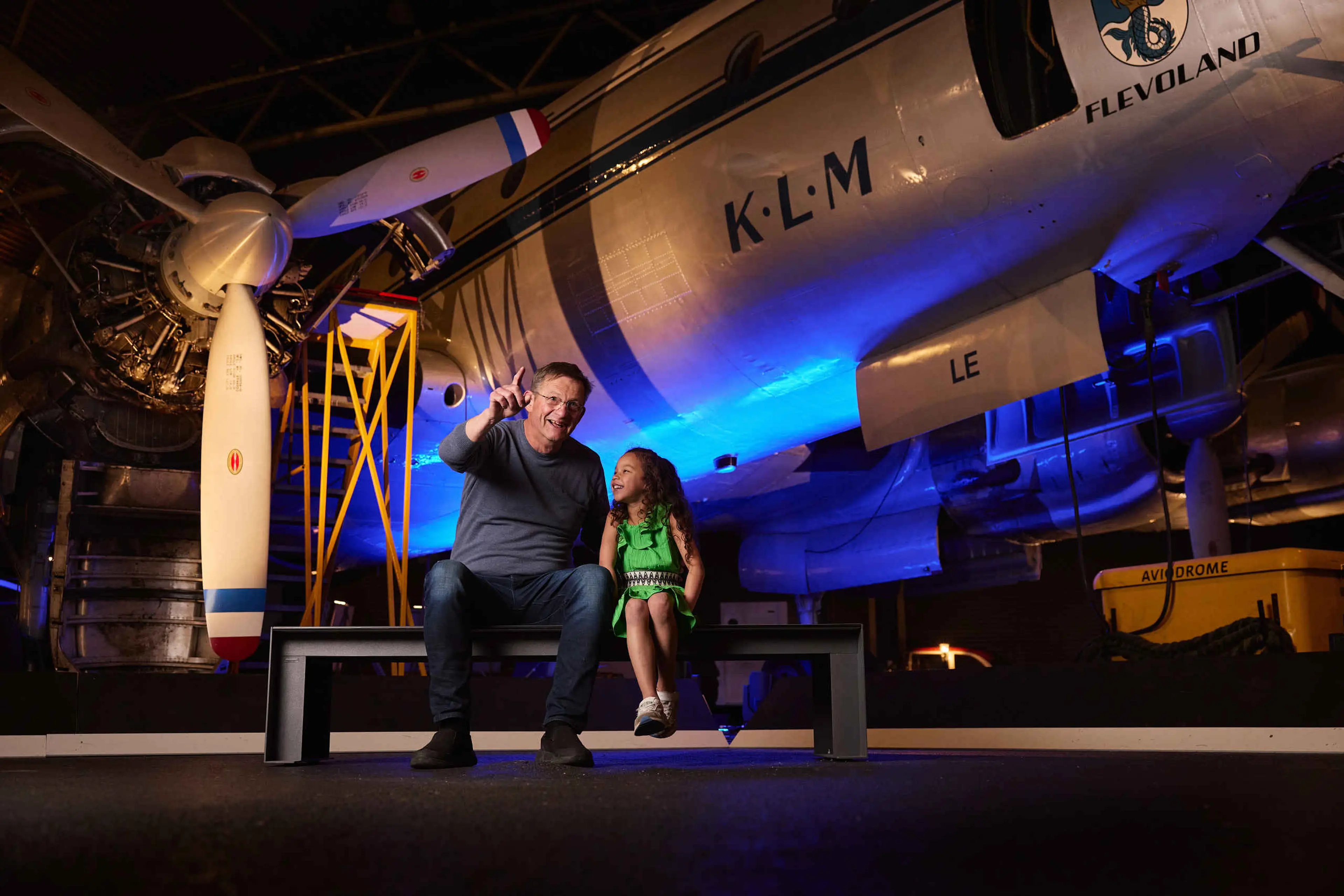 Een opa en kleindochter zitten op een bankje in de binnenexpositie van Luchtvaartmuseum Aviodrome