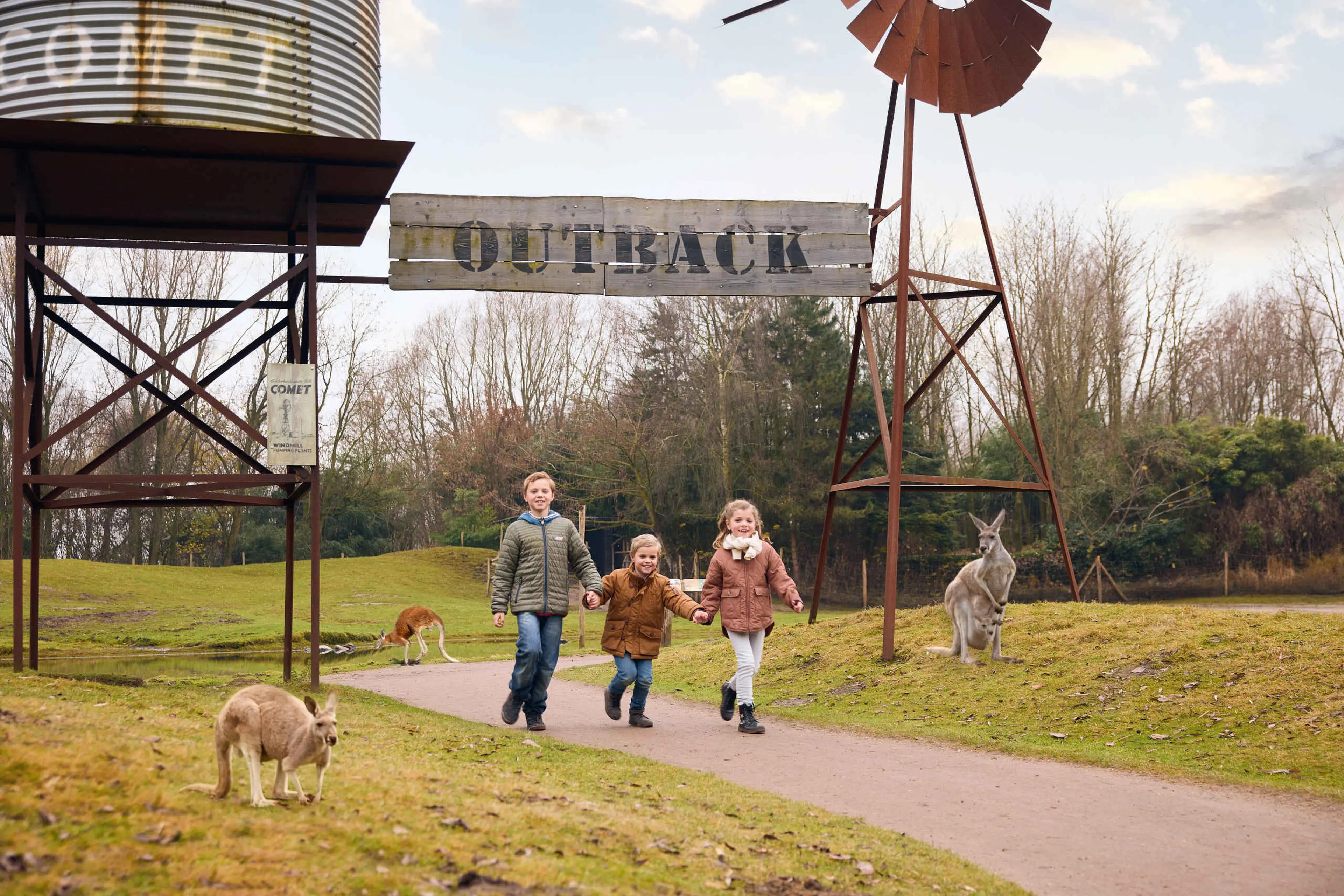Drie kinderen lopen door de Outback met kangoeroe's op de achtergrond in ZooParc Overloon