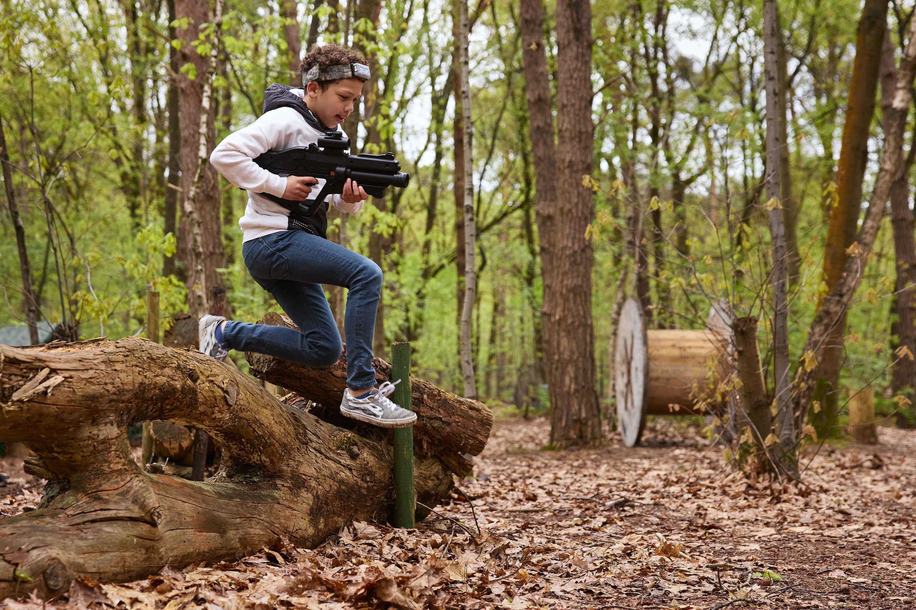 Een jongen springt over een boomstam tijdens het outdoor lasergamen bij Klimrijk Brabant.