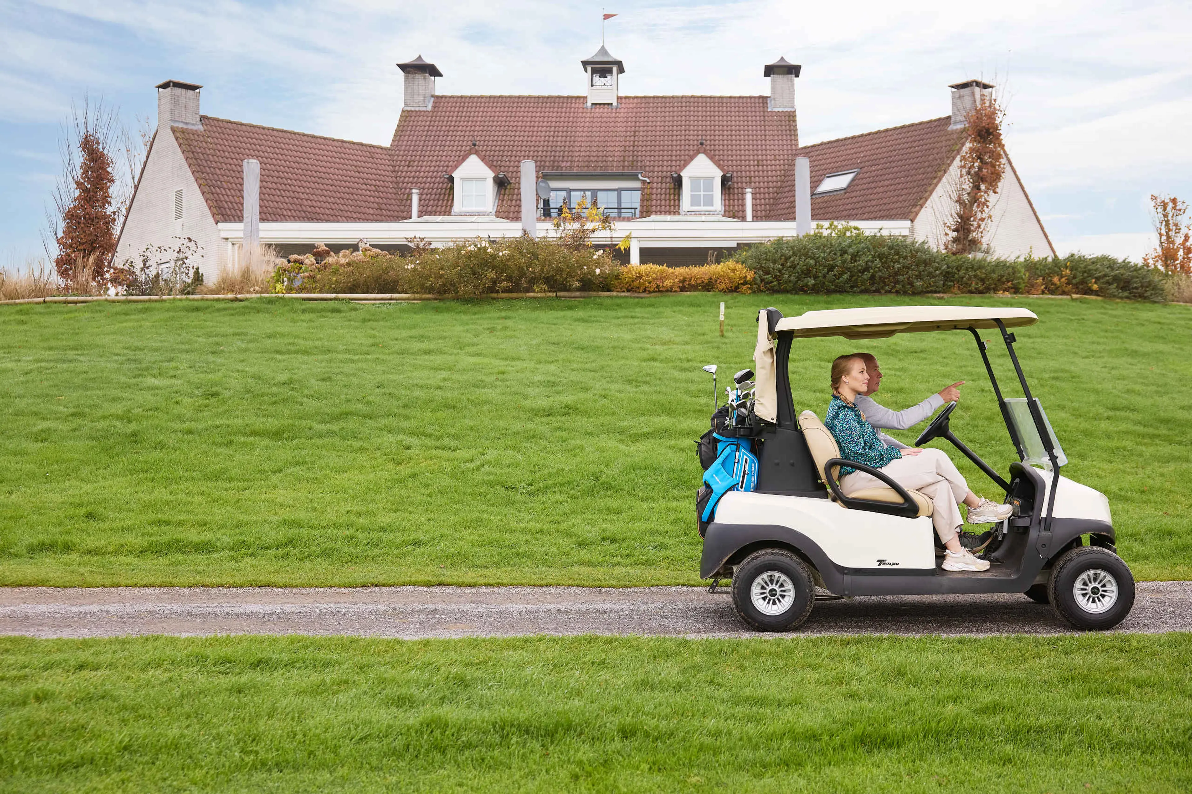 Vader en dochter in golfkar met restaurant De Hooghe Bergh op de achtergrond bij Golf De Gulbergen