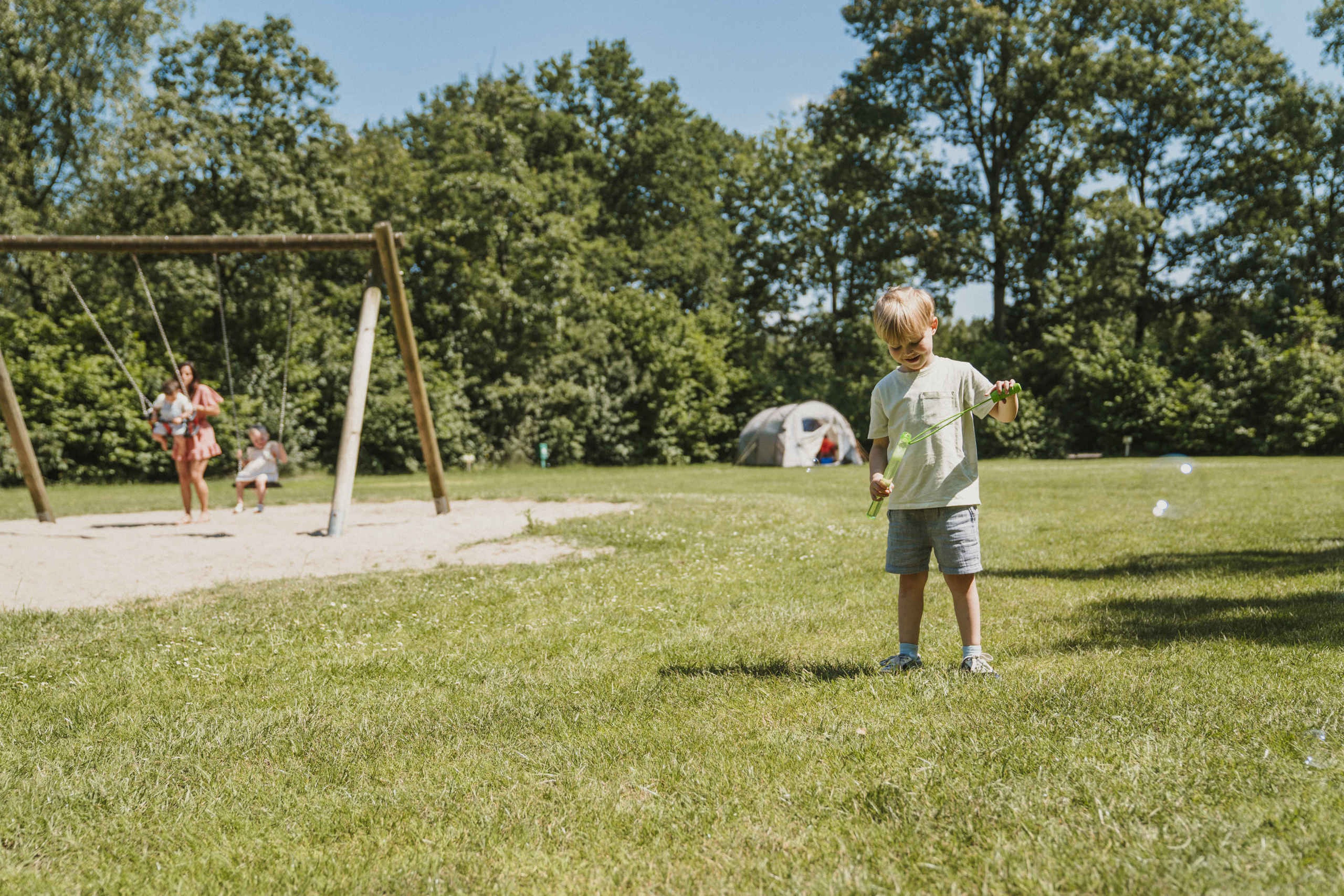Een gezin is aan het schommelen terwijl een jongen bellen blaast op de kampeerplaats bij Vakantiepark Dierenbos
