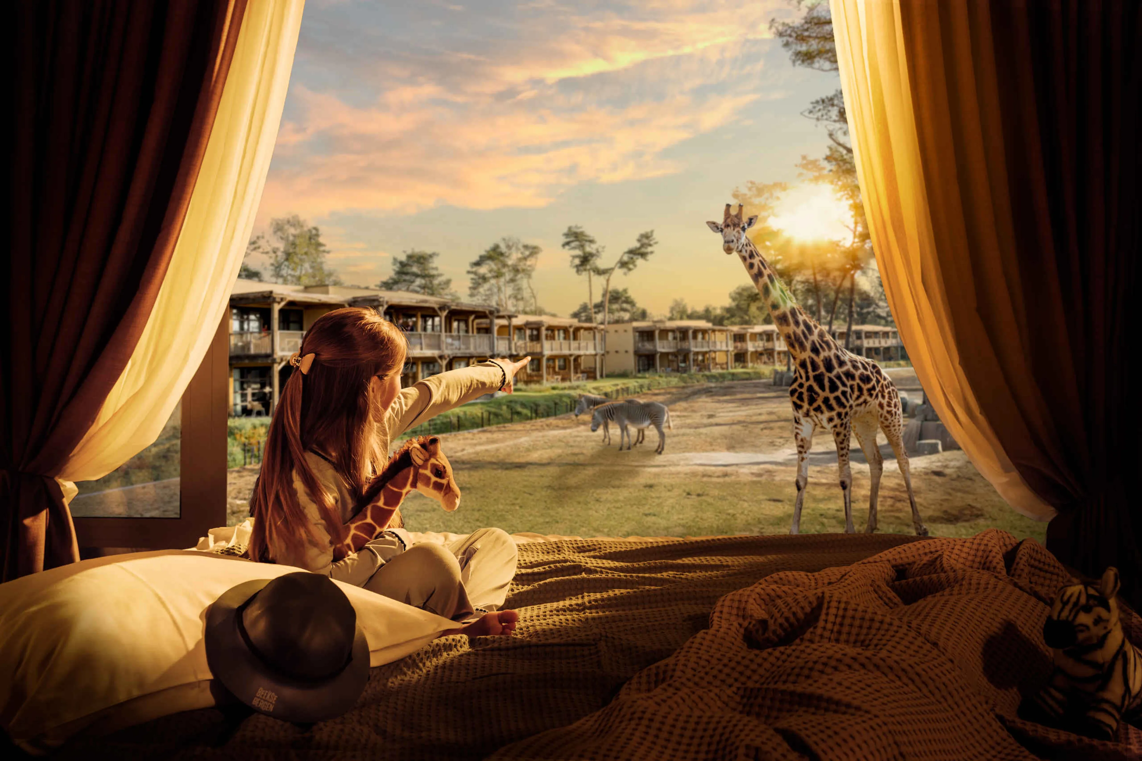 Meisje kijkt vanuit bed naar giraffe in Safari Hotel Beekse Bergen