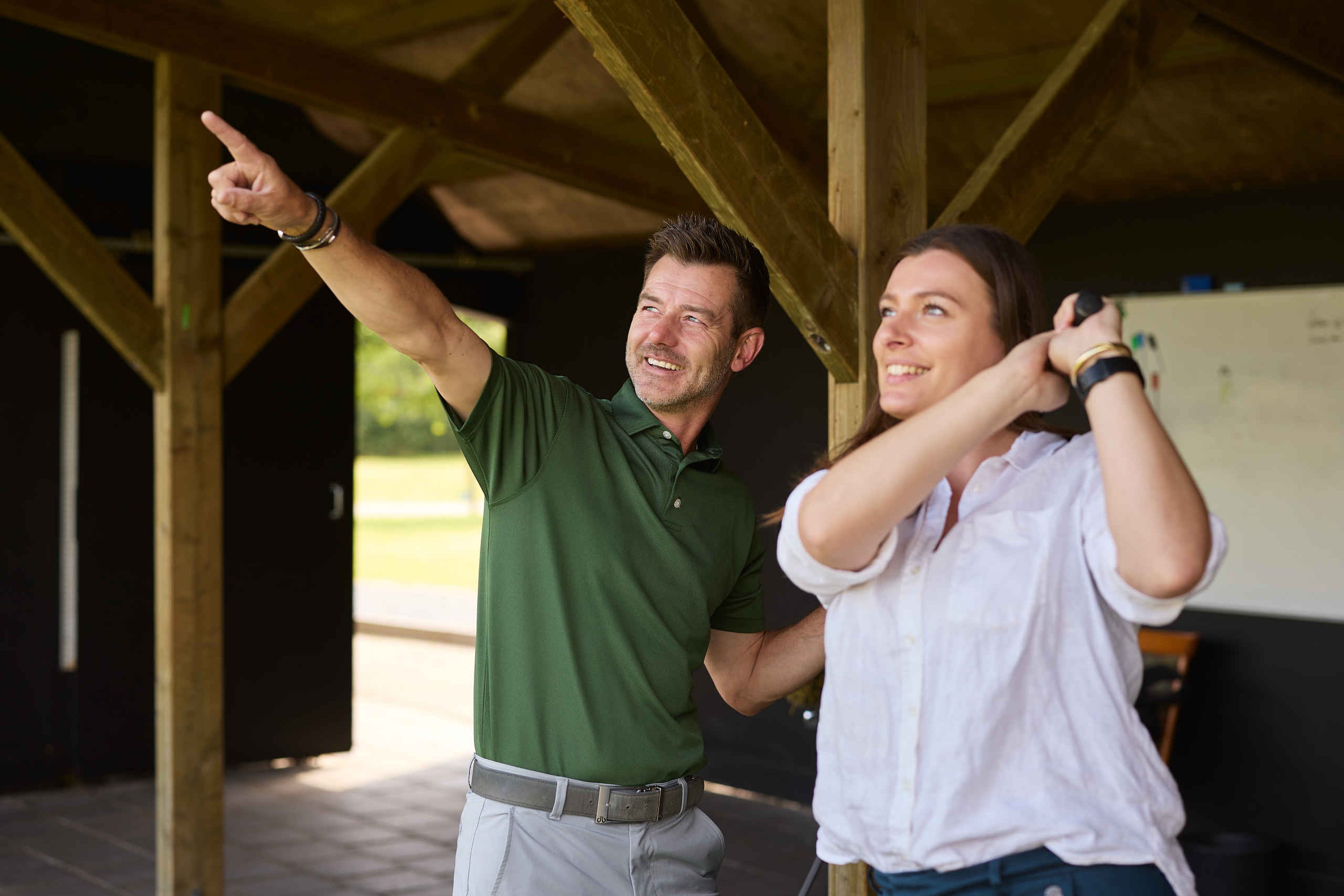 De golfpro van de Golfacademy geeft uitleg aan een vrouw op de driving range van Golf De Gulbergen