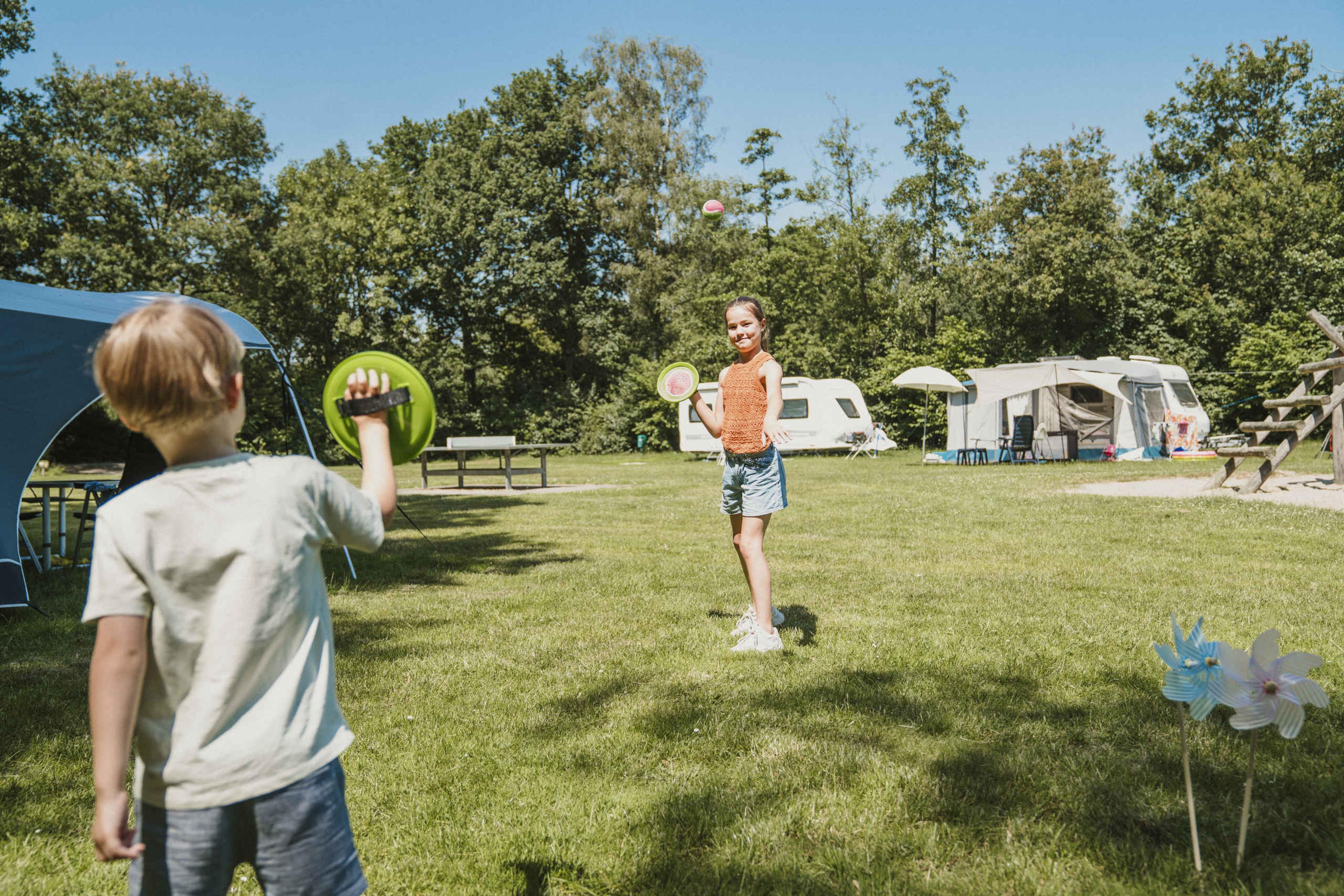 Een meisje en een jongen spelen tennis op de kampeerplaats bij Vakantiepark Dierenbos