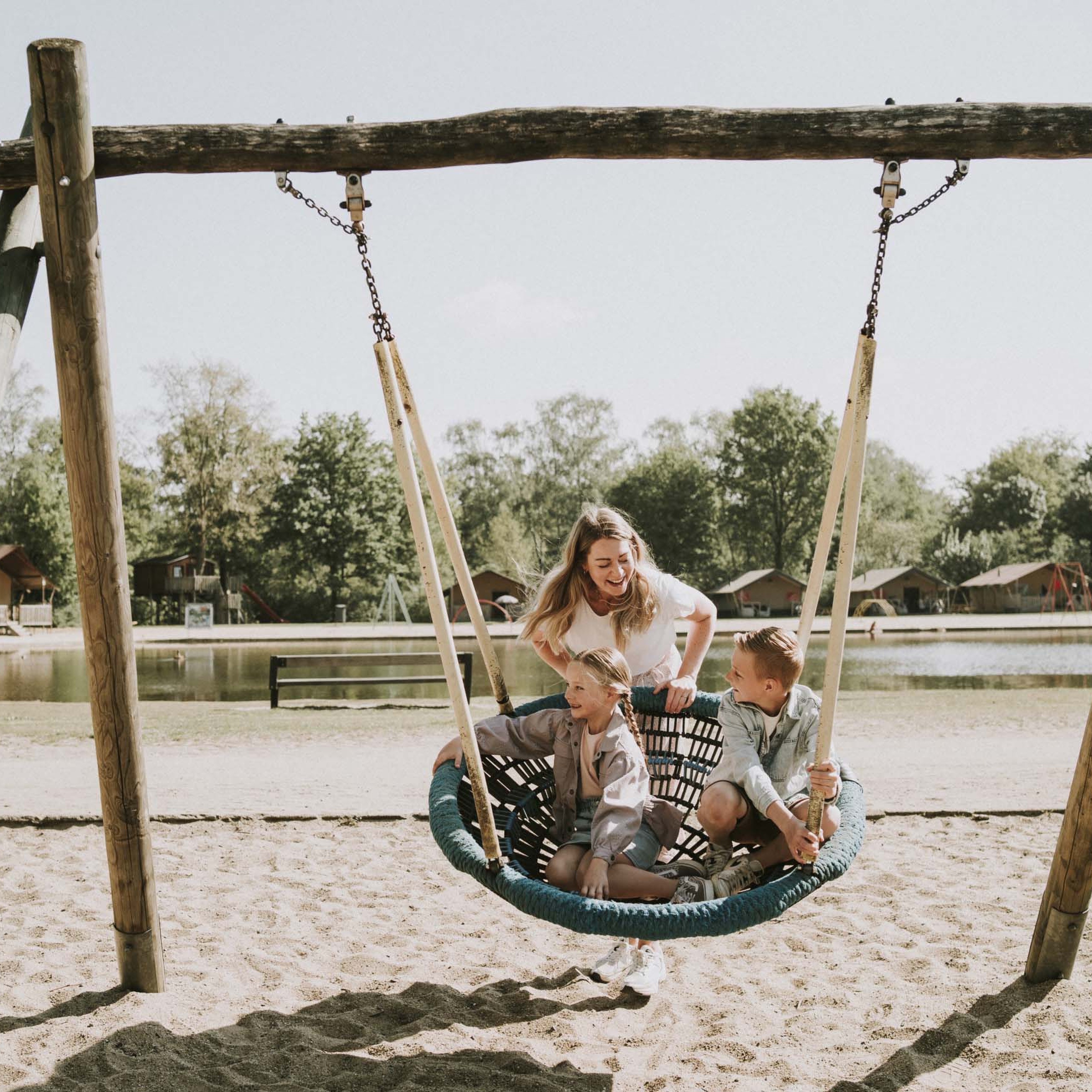 Moeder en kinderen spelen met een schommel in de speeltuin van Vakantiepark Dierenbos