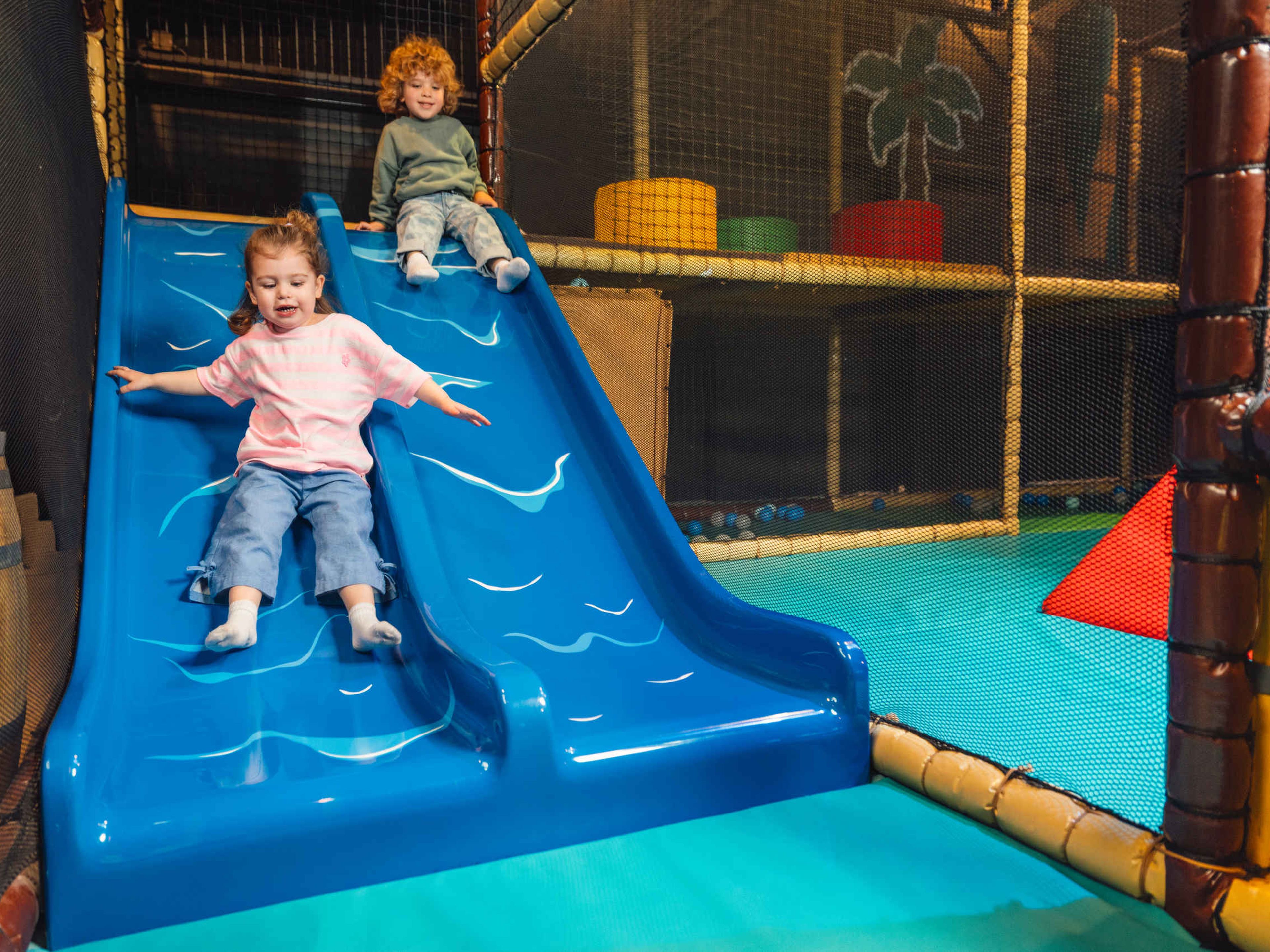 Twee kleuters glijden van de kleine glijbaan bij Speelland Indoor
