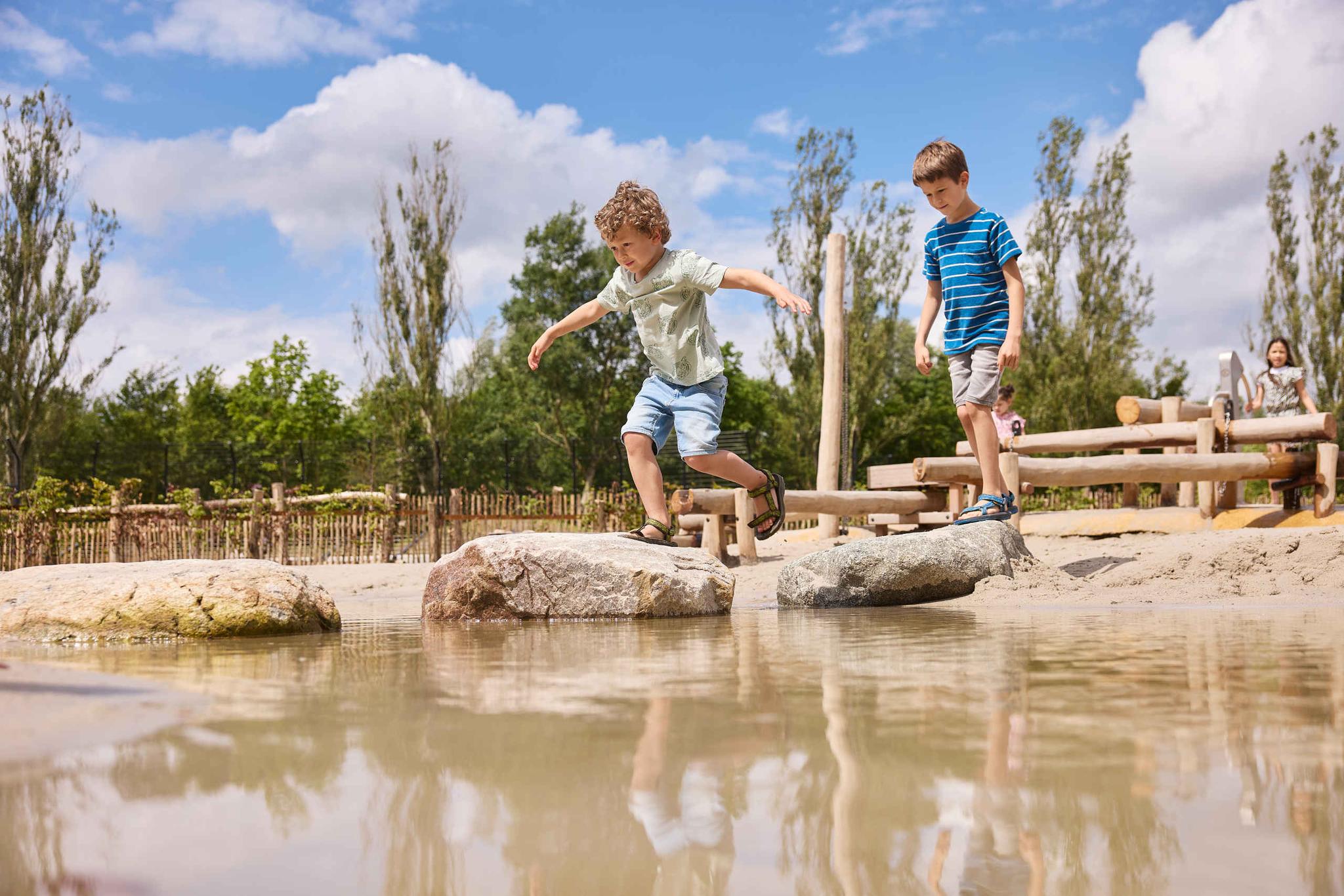 Twee jongens lopen over de stenen in het water bij de waterspeeltuin in Eindhoven Zoo.