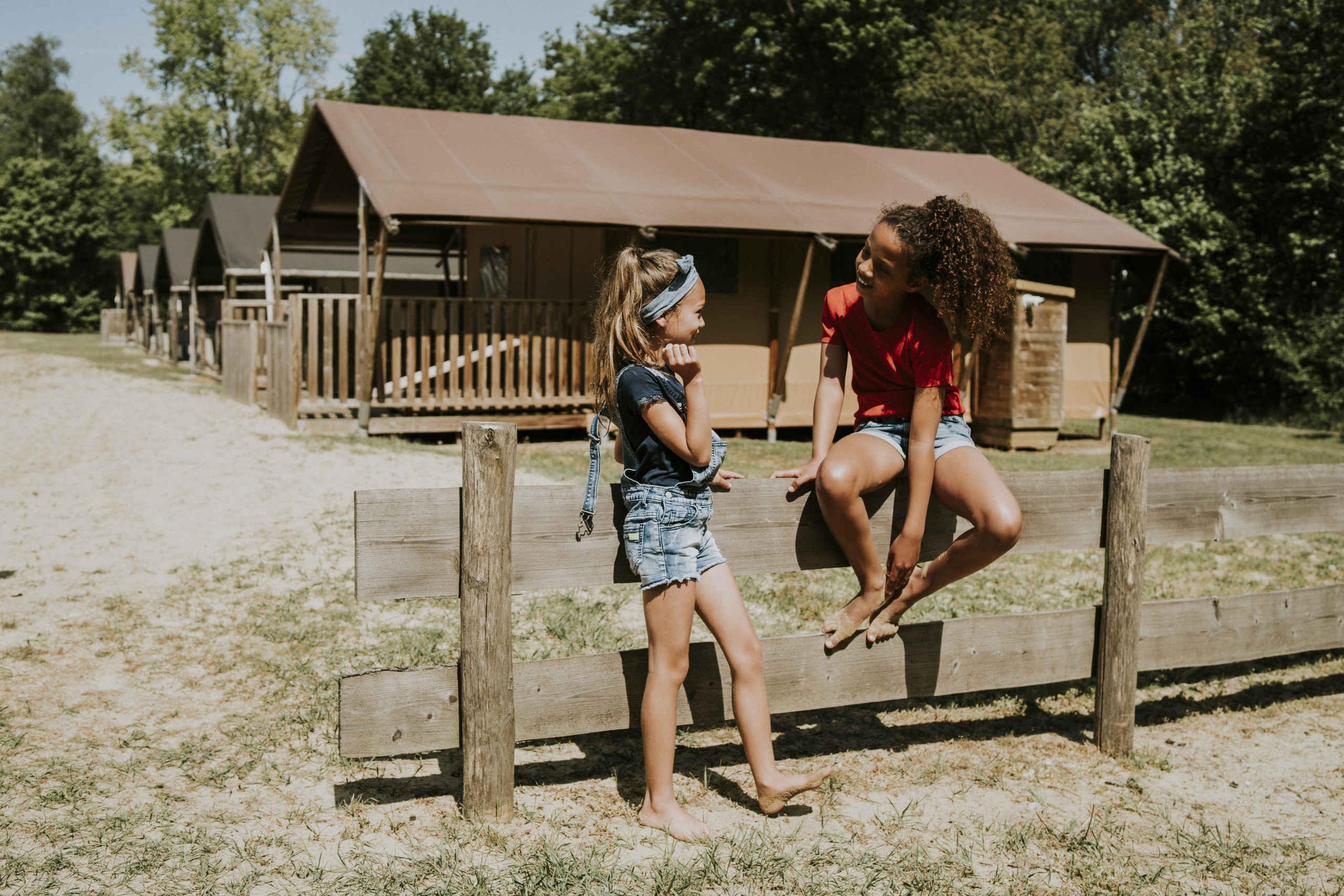 Kinderen zitten op een hekje bij de Luxe Lodgetent Pauw op Vakantiepark Dierenbos