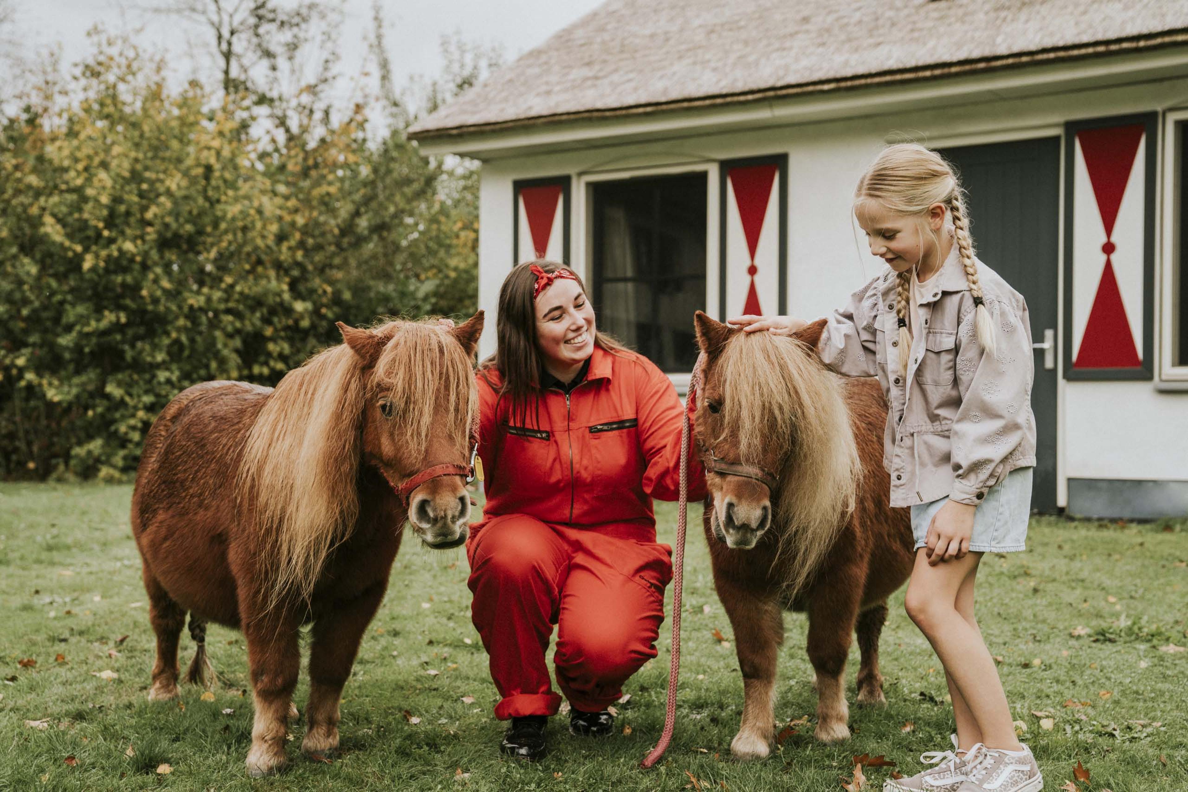 Dierenverzorger en meisje aaien pony's in de kinderboerderij van Vakantiepark Dierenbos