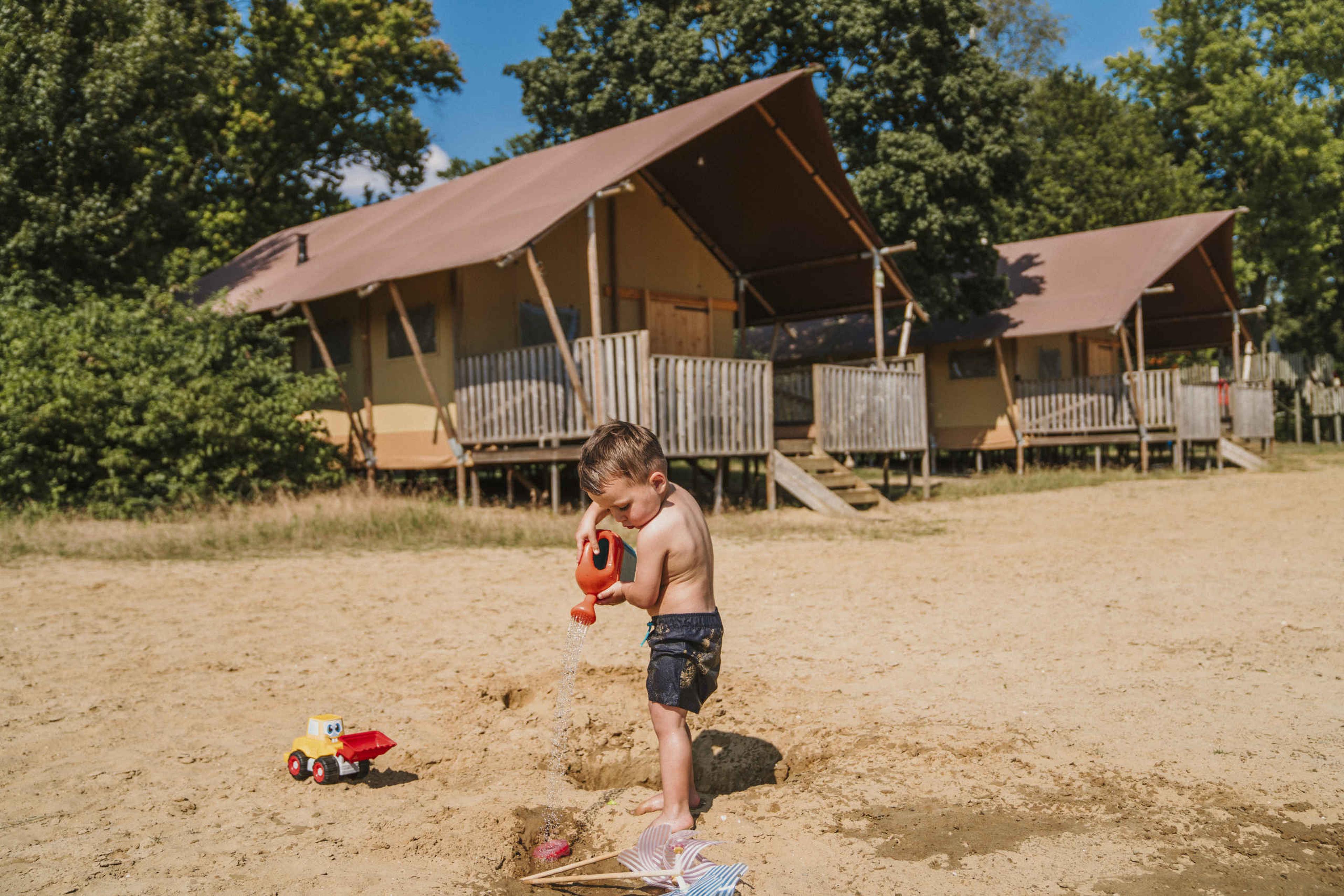 Een jongen speelt op het zandstrand voor de lodgetent pauw aan de zwemvijver bij Vakantiepark Dierenbos