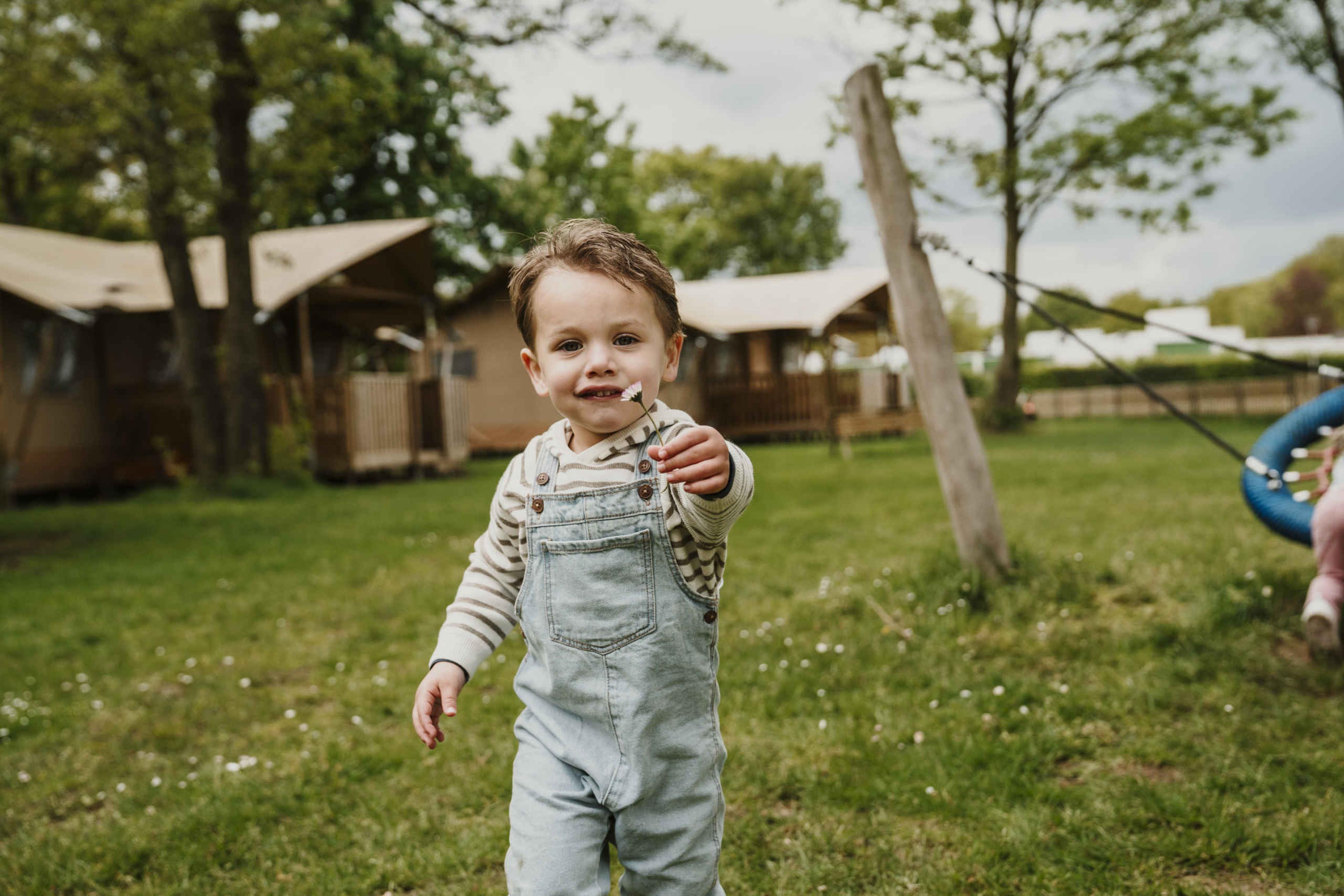Een jongen met een bloem bij de Lodge tenten op Vakantiepark Dierenbos.