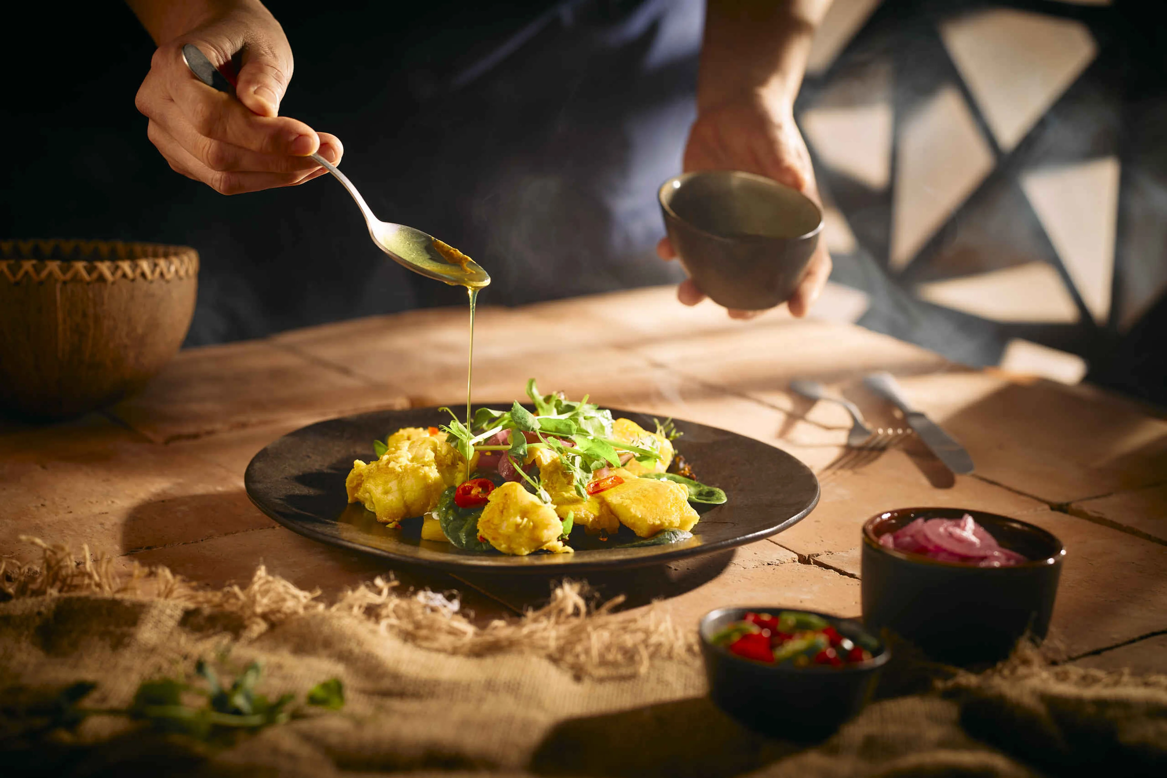 De chef giet saus over een visgerecht met kerrie bij restaurant Moto in Safari Resort Beekse Bergen.