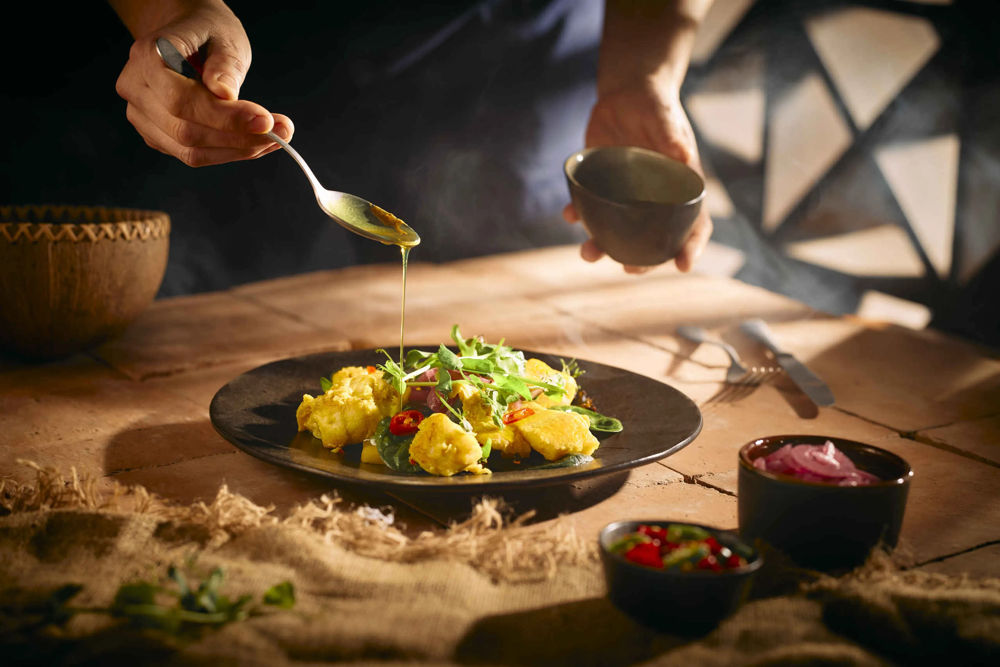 De chef giet saus over een visgerecht met kerrie bij restaurant Moto in Safari Resort Beekse Bergen.