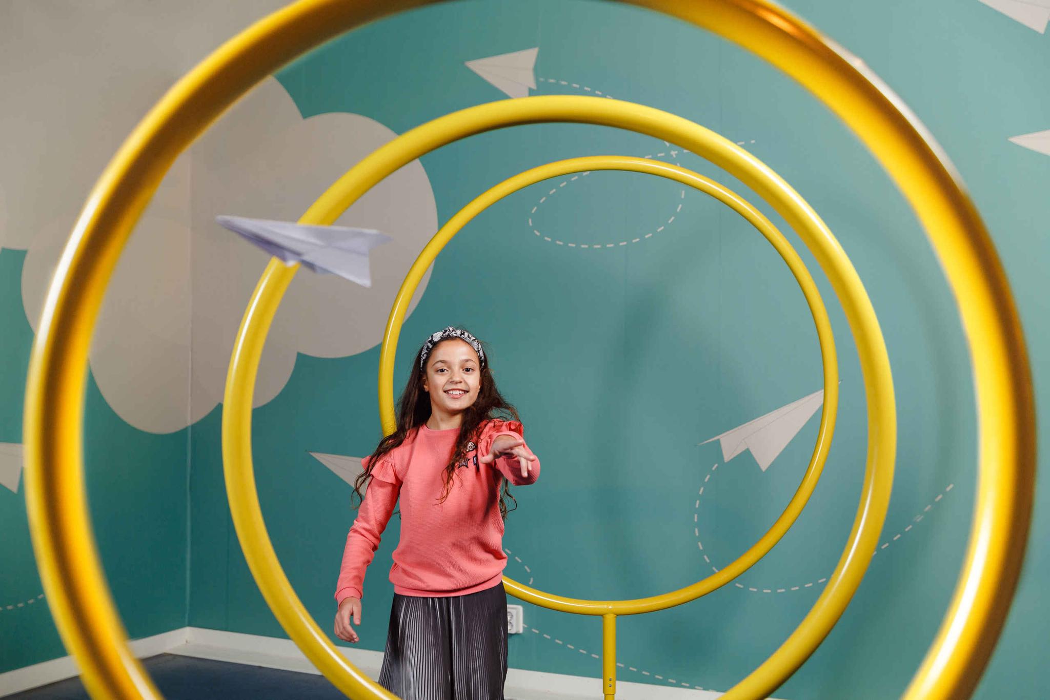 Een meisje gooit een papieren vliegtuigje in Luchtvaartmuseum Aviodrome