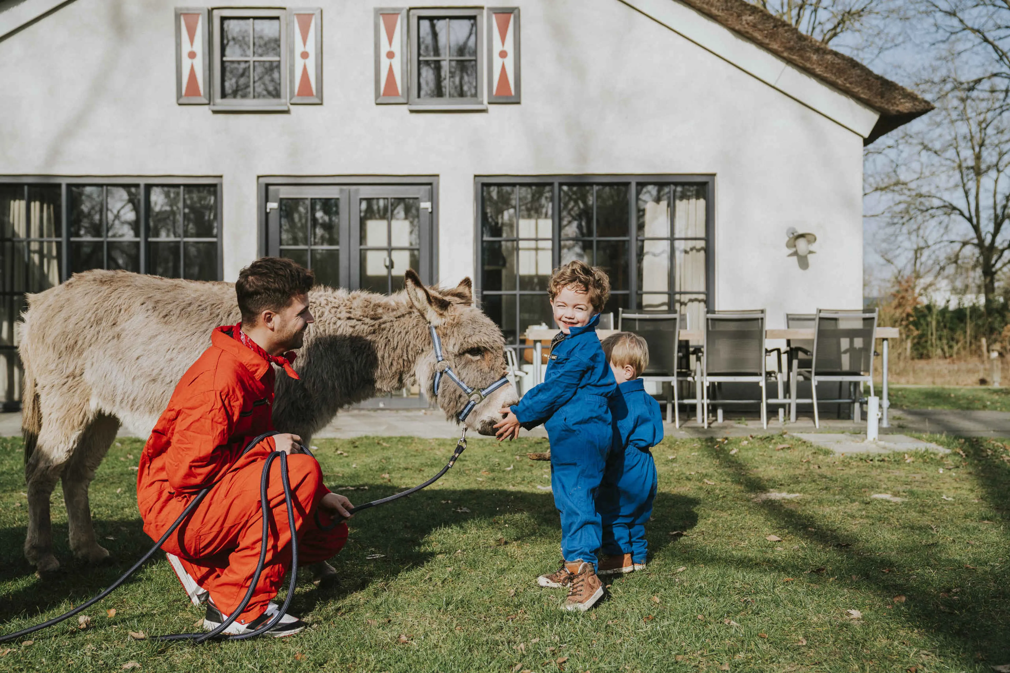 Twee kinderen kijken bij een ezel met de dierenverzorger.