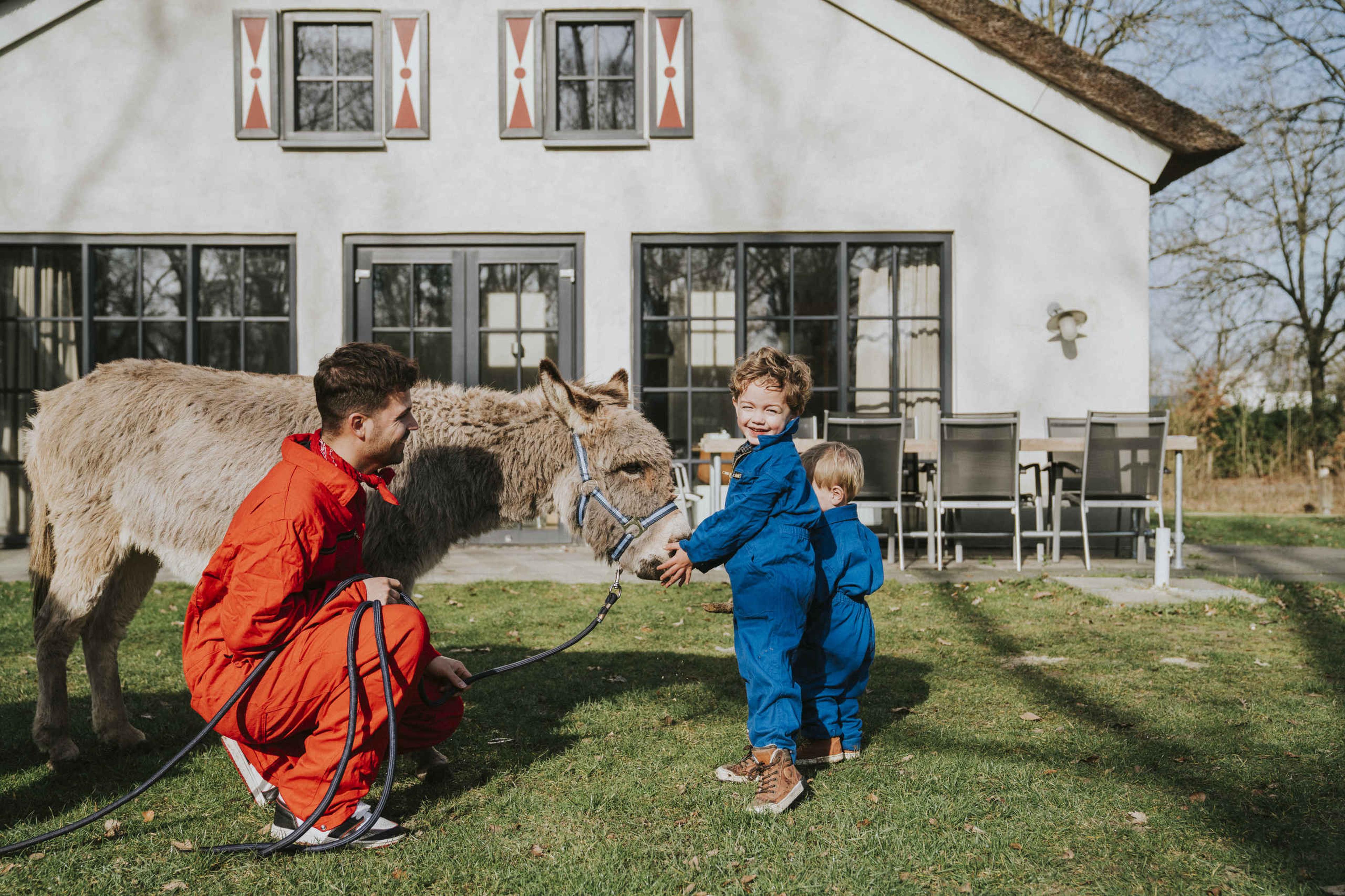 Twee kinderen kijken bij een ezel met de dierenverzorger.