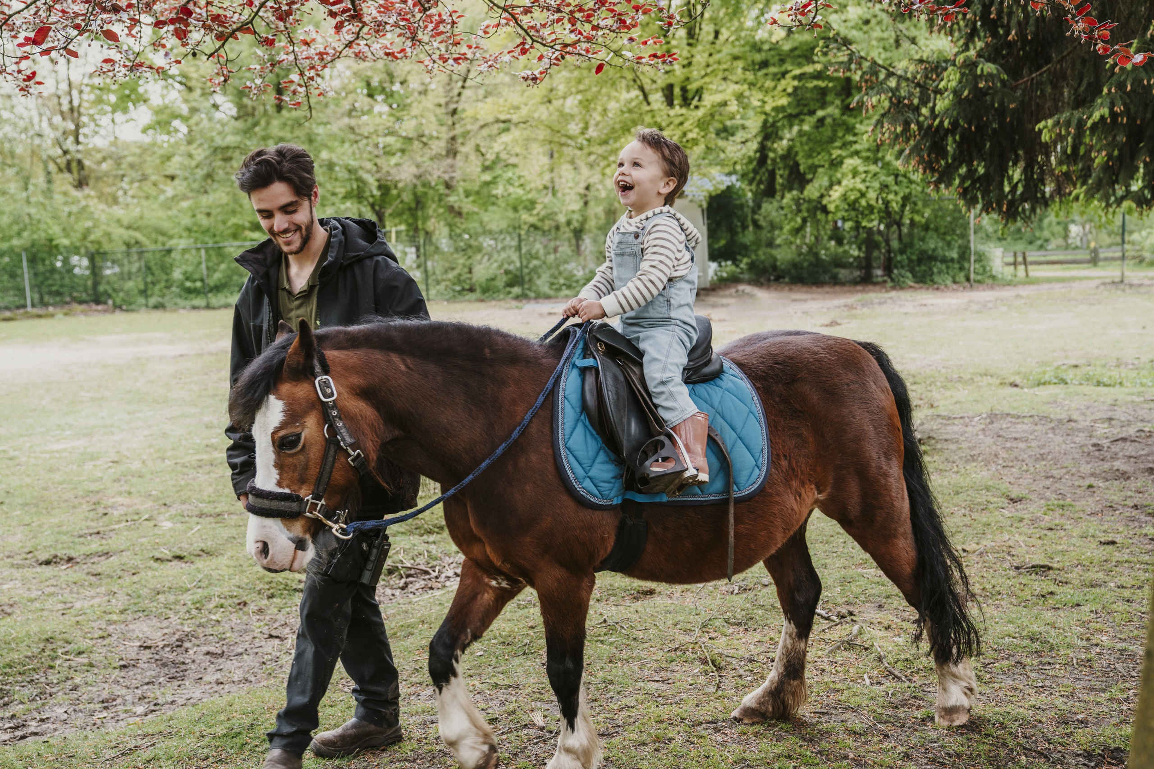 Jongen rijdt paard met begeleider en lacht bij Vakantiepark Dierenbos