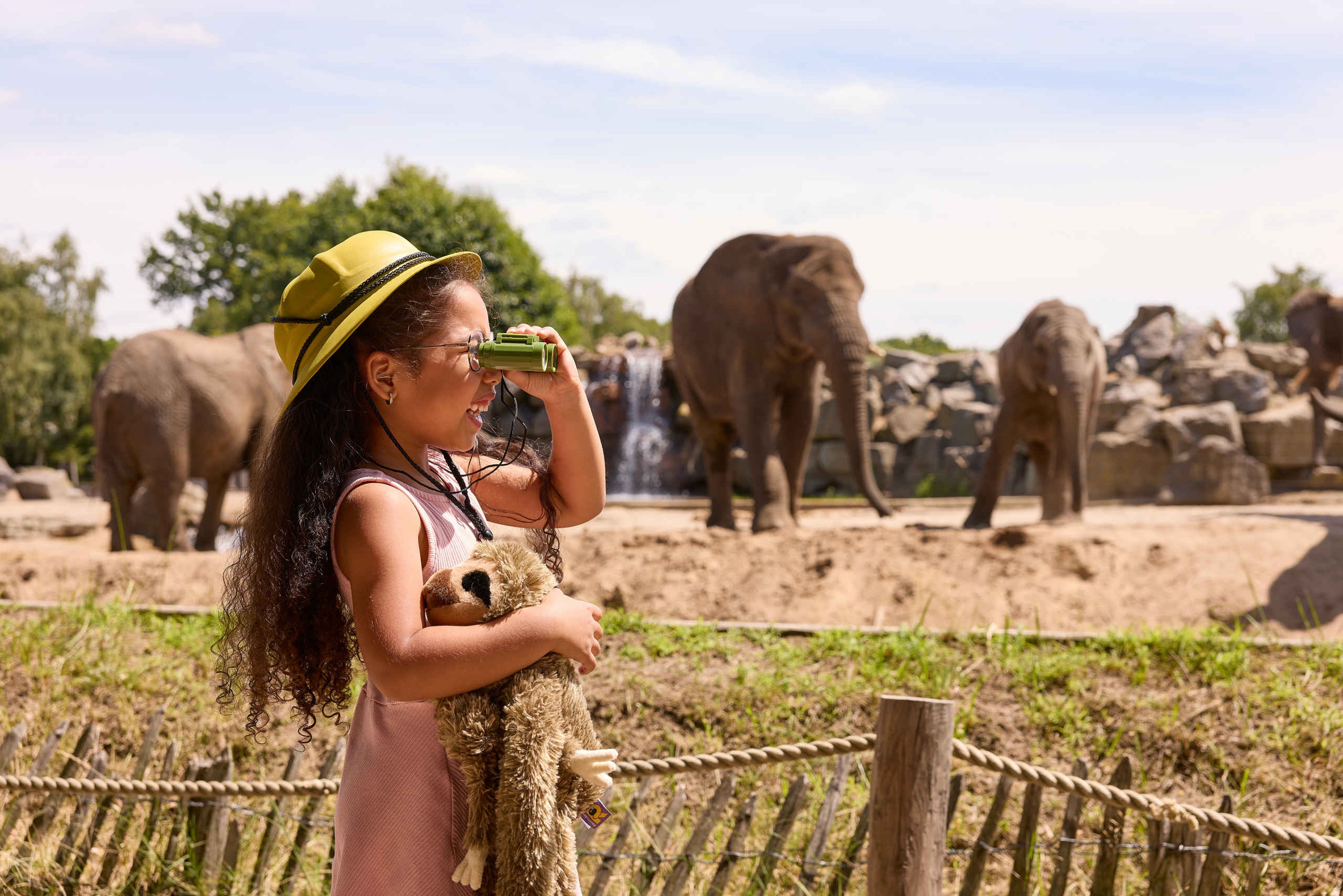 Meisje in de zomer met verrekijker en knuffel bij olifanten in Safaripark Beekse Bergen