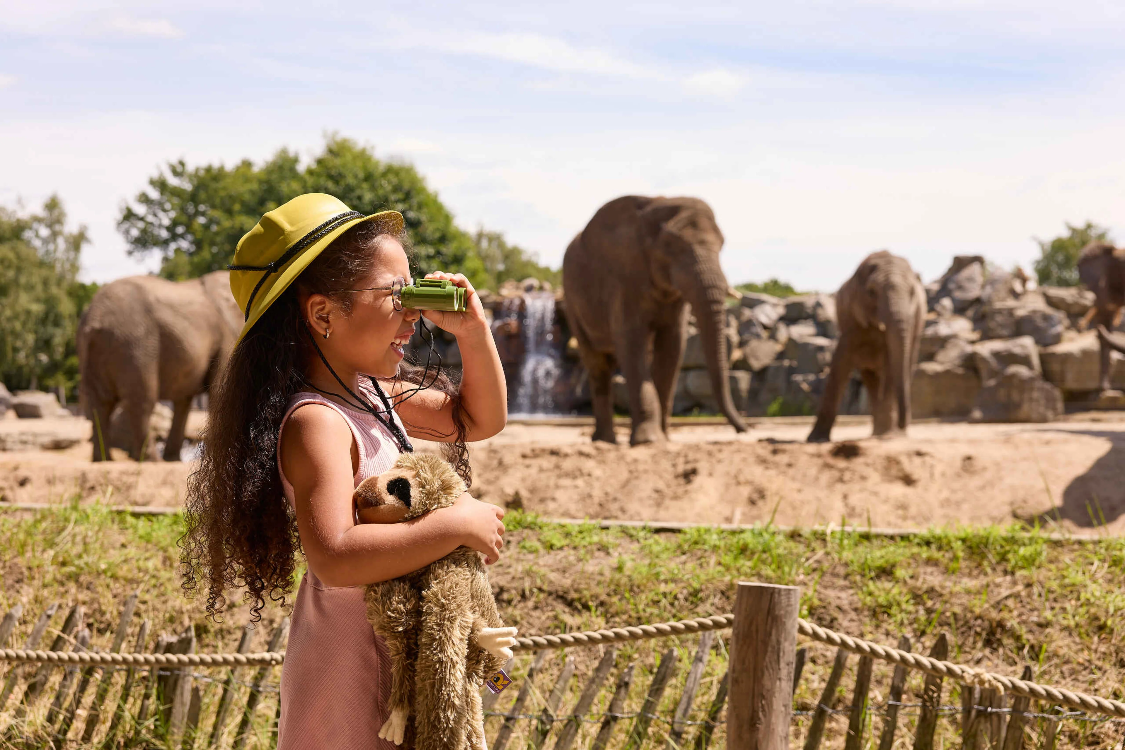 Meisje in de zomer met verrekijker en knuffel bij olifanten in Safaripark Beekse Bergen