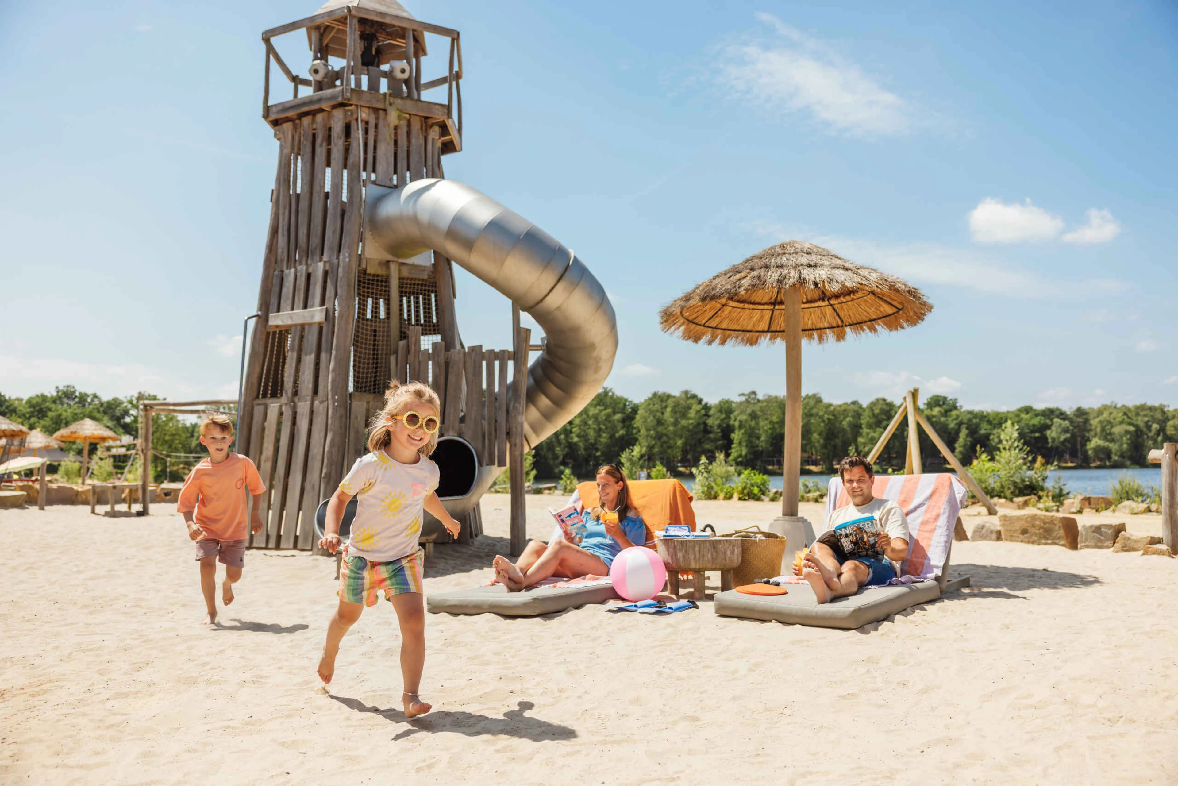 Twee kinderen spelen op het strand van Bojo Beach terwijl hun ouders ontspannen op de ligbedden bij Lake Resort Beekse Bergen.
