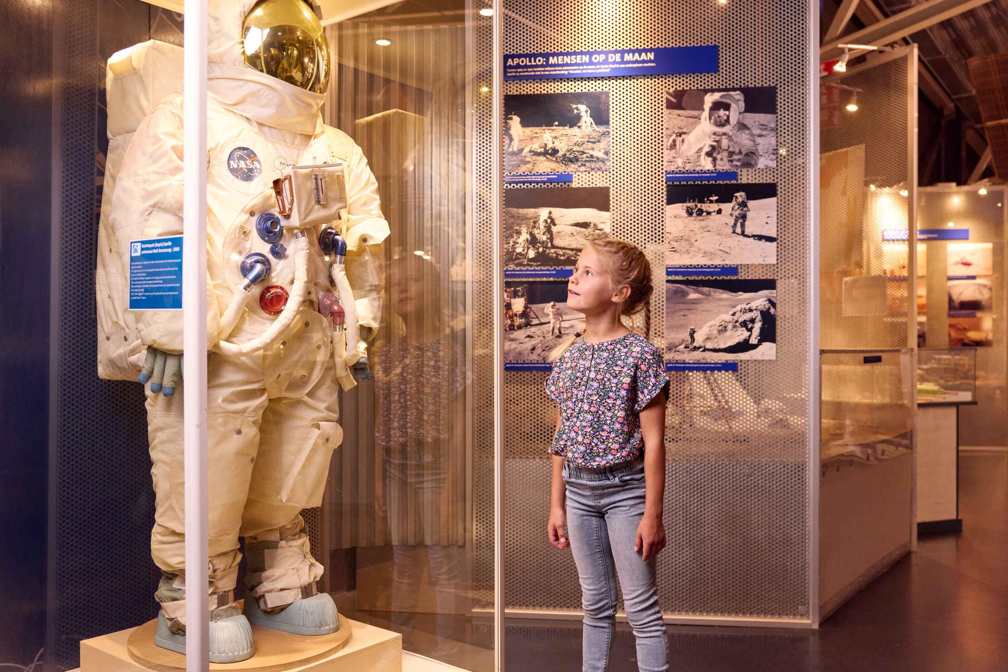 Een meisje naast een astronautenpak in de ruimtevaartexpositie van Luchtvaartmuseum Aviodrome