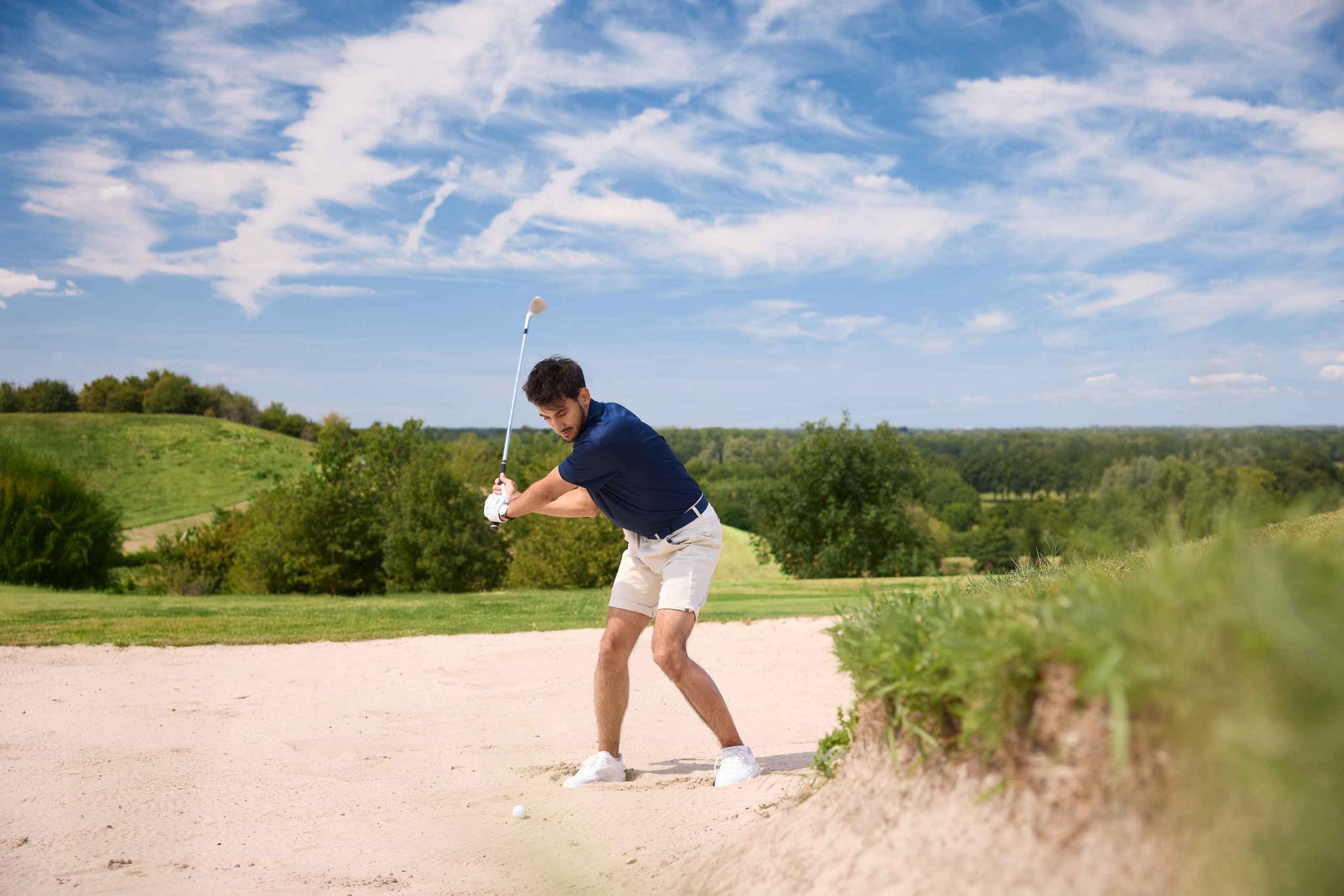 Een man maakt een achterzwaai om een bal uit de bunker te slaan op de Sprookjesbaan van Golf De Gulbergen
