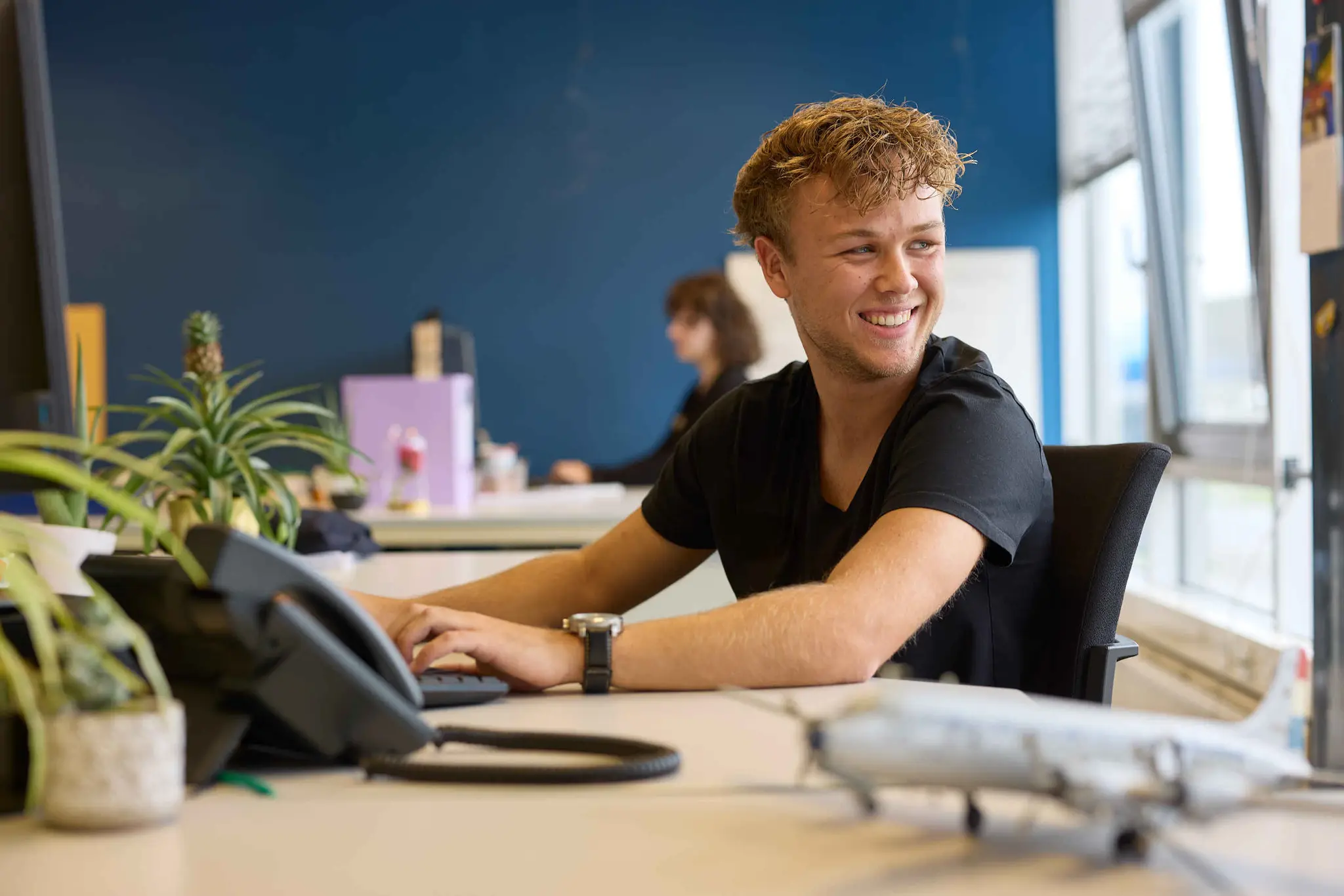 een man zit aan zijn bureau met daarop een telefoon en vliegtuig bij Luchtvaartmuseum Aviodrome