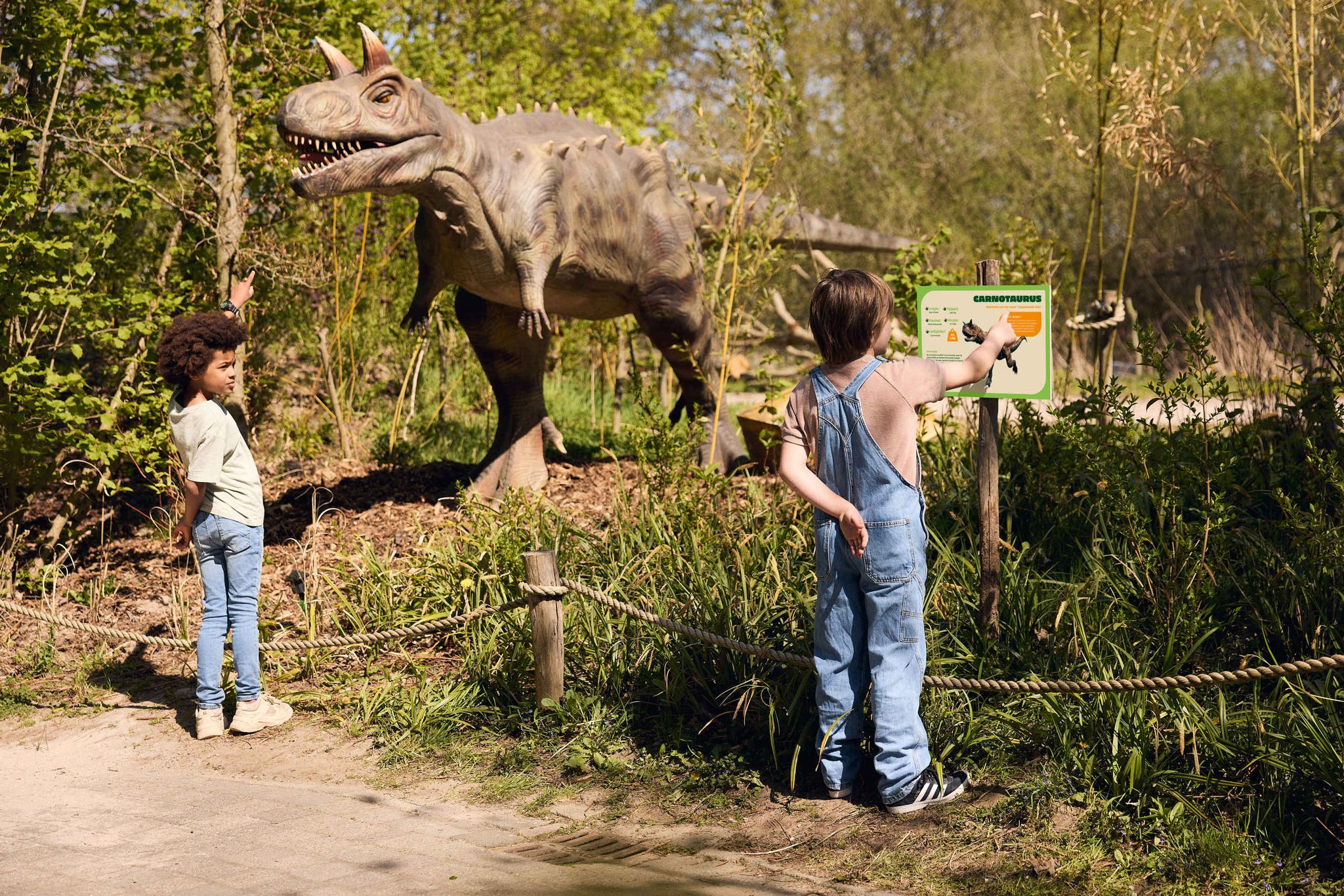 Twee kinderen kijken naar een dino met informatiebord bij DINO vs DIER in Eindhoven Zoo.